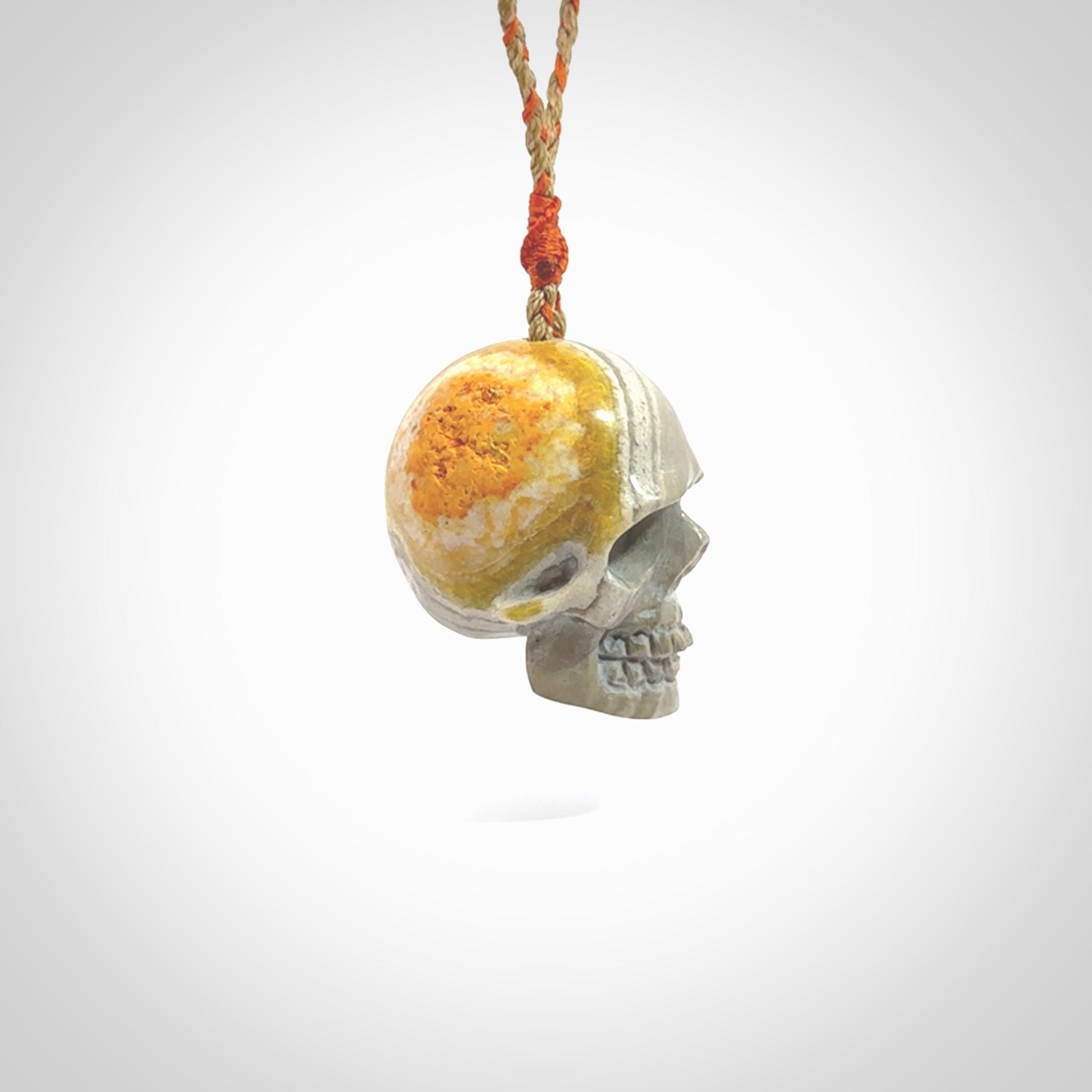 This picture shows a large sized Bumblebee Jasper stone skull pendant that we have hand carved. It is polished to a soft shine and is a very striking piece. The cord is a orange and tan colour and has a small orange floret binding just above the pendant.