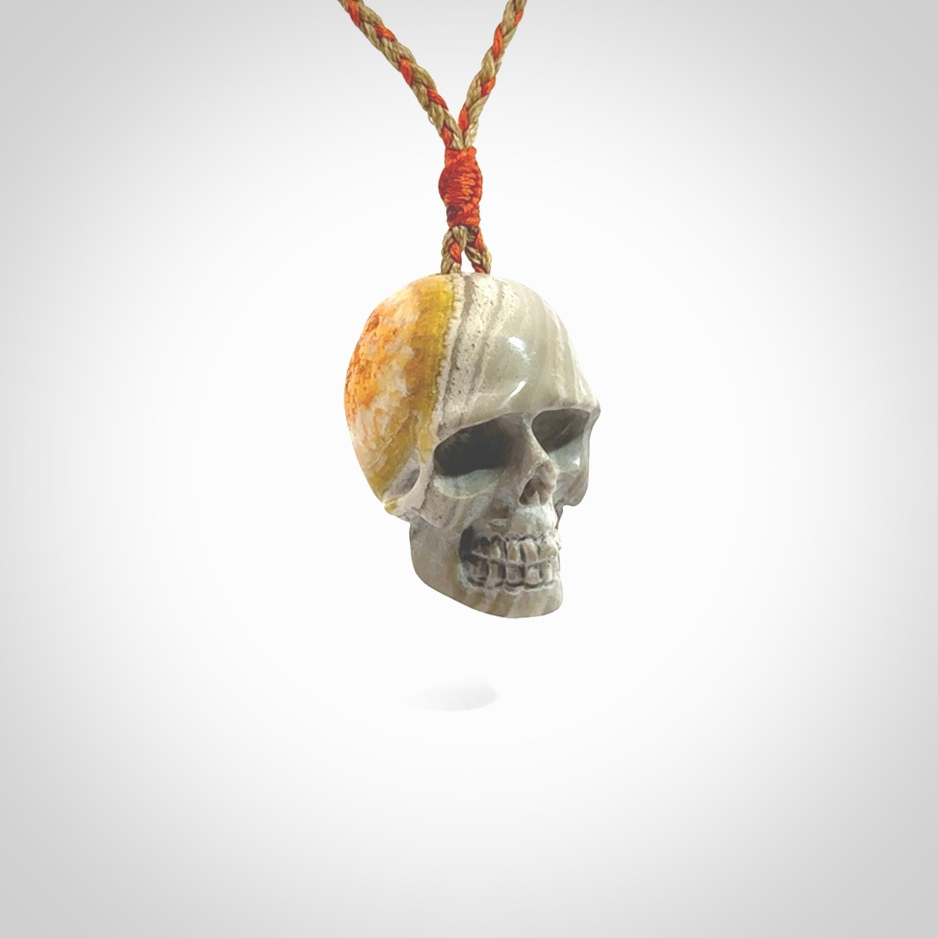 This picture shows a large sized Bumblebee Jasper stone skull pendant that we have hand carved. It is polished to a soft shine and is a very striking piece. The cord is a orange and tan colour and has a small orange floret binding just above the pendant.