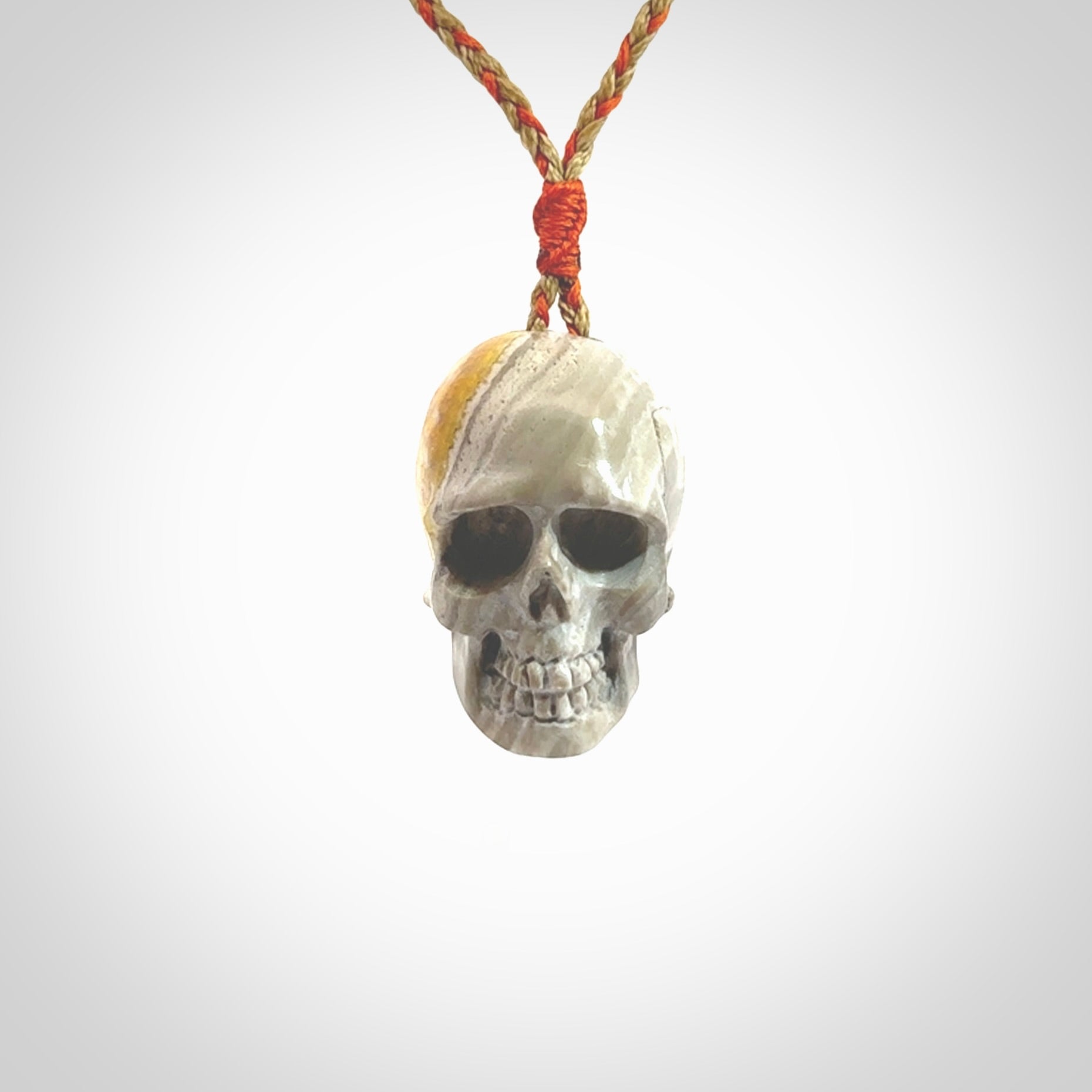 This picture shows a large sized Bumblebee Jasper stone skull pendant that we have hand carved. It is polished to a soft shine and is a very striking piece. The cord is a orange and tan colour and has a small orange floret binding just above the pendant.