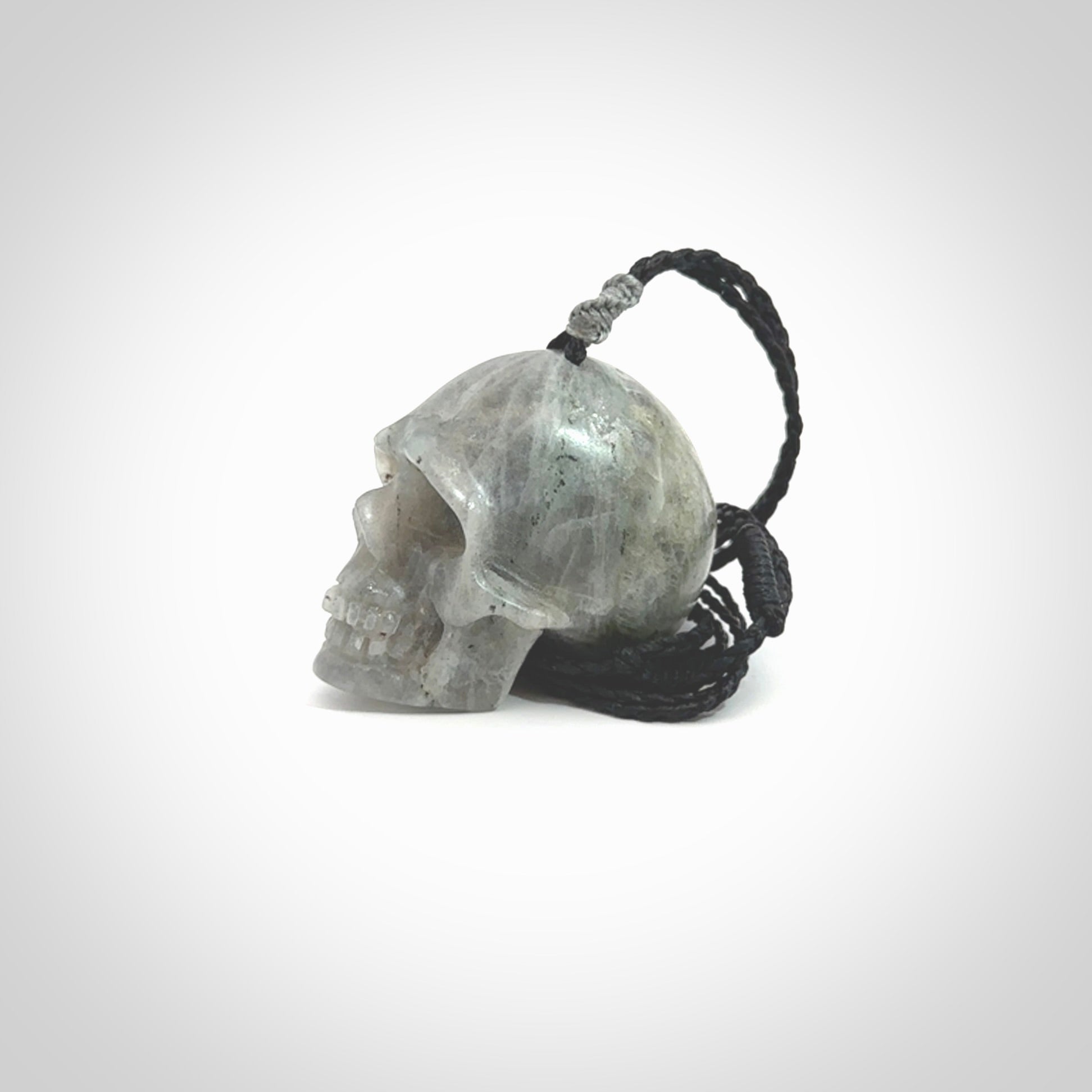 This picture shows a large sized Grey Moonstone skull pendant that we have hand carved. It is polished to a soft shine and is a very striking piece. The cord is black and has a small grey floret binding just above the pendant.