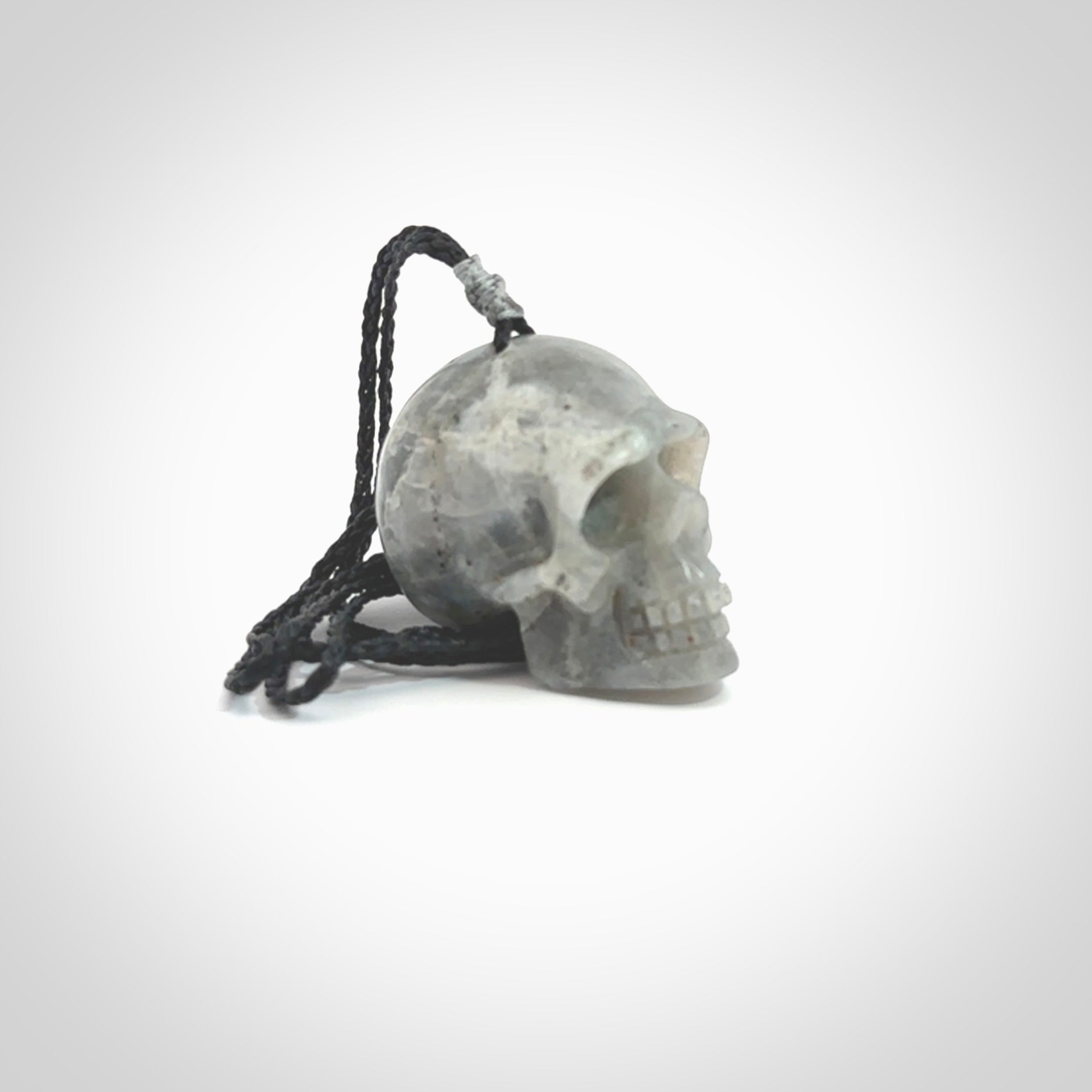 This picture shows a large sized Grey Moonstone skull pendant that we have hand carved. It is polished to a soft shine and is a very striking piece. The cord is black and has a small grey floret binding just above the pendant.