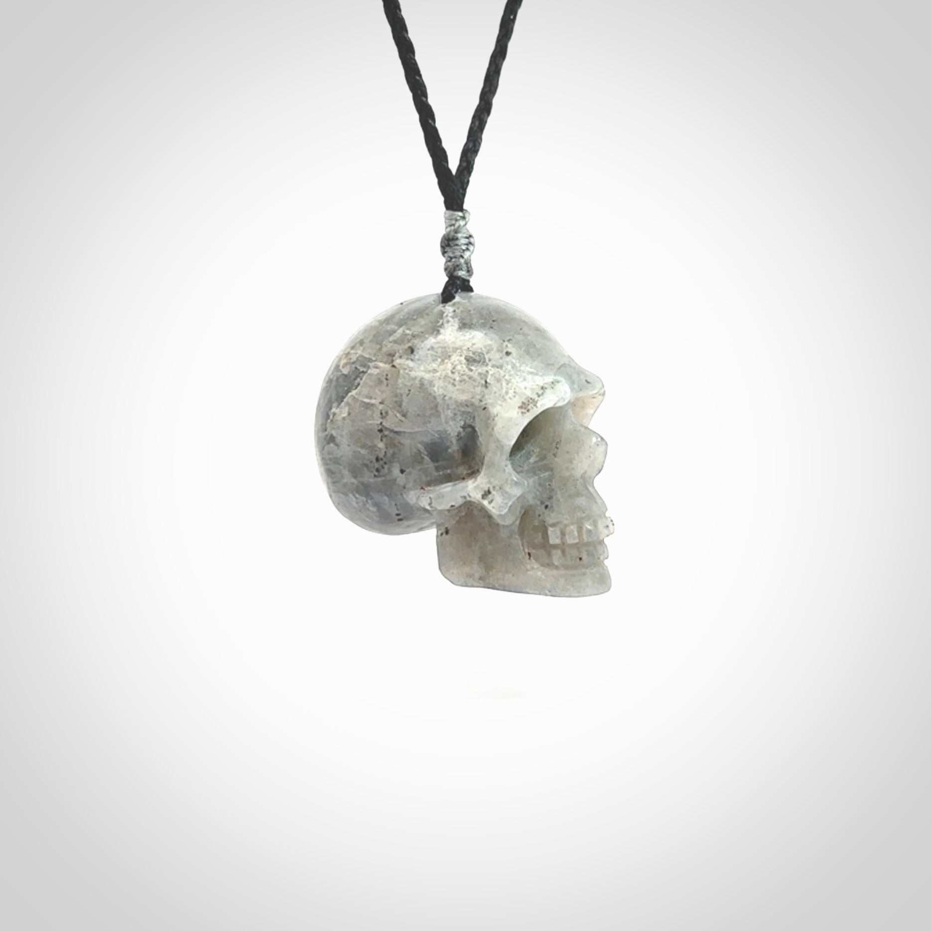 This picture shows a large sized Grey Moonstone skull pendant that we have hand carved. It is polished to a soft shine and is a very striking piece. The cord is black and has a small grey floret binding just above the pendant.