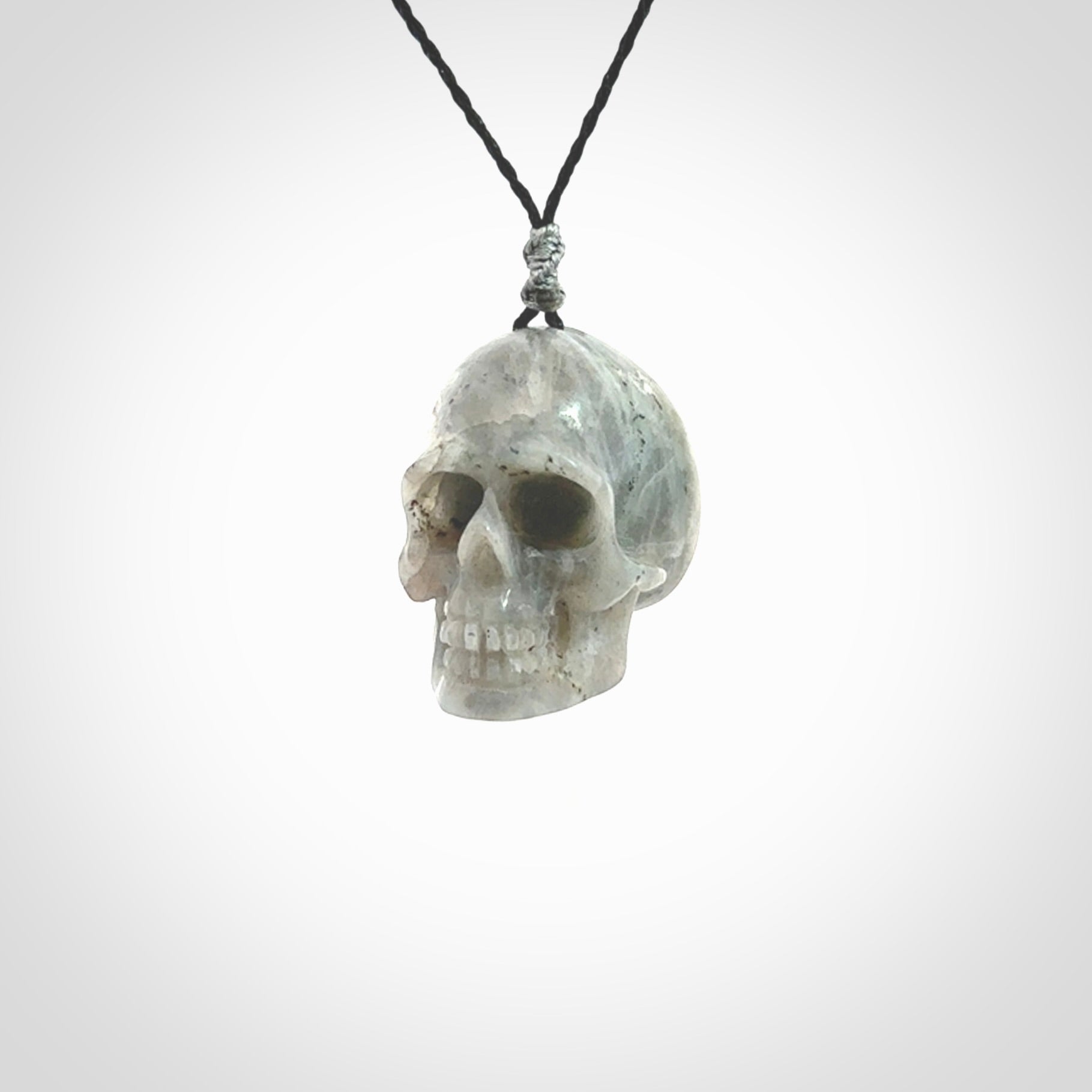 This picture shows a large sized Grey Moonstone skull pendant that we have hand carved. It is polished to a soft shine and is a very striking piece. The cord is black and has a small grey floret binding just above the pendant.