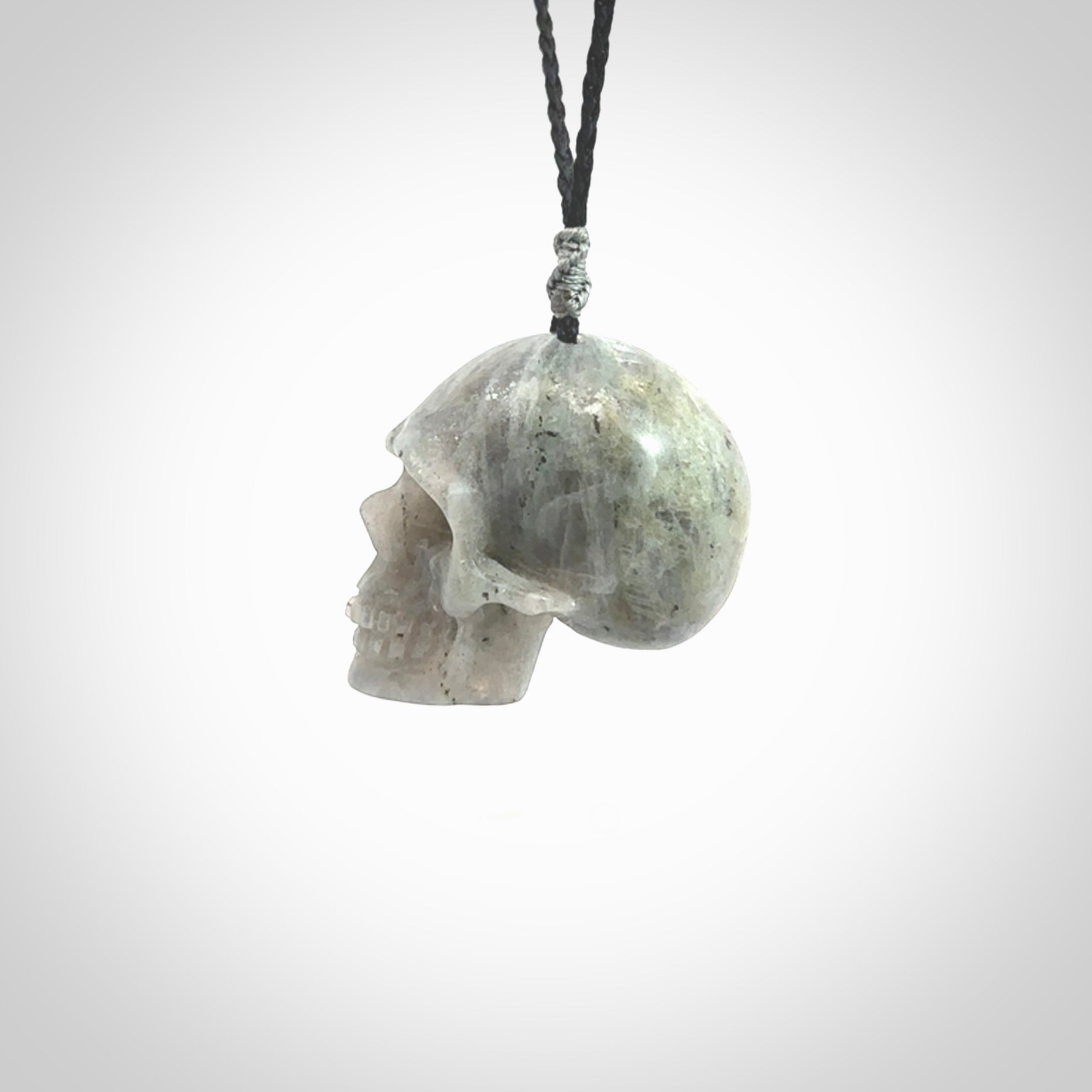 This picture shows a large sized Grey Moonstone skull pendant that we have hand carved. It is polished to a soft shine and is a very striking piece. The cord is black and has a small grey floret binding just above the pendant.