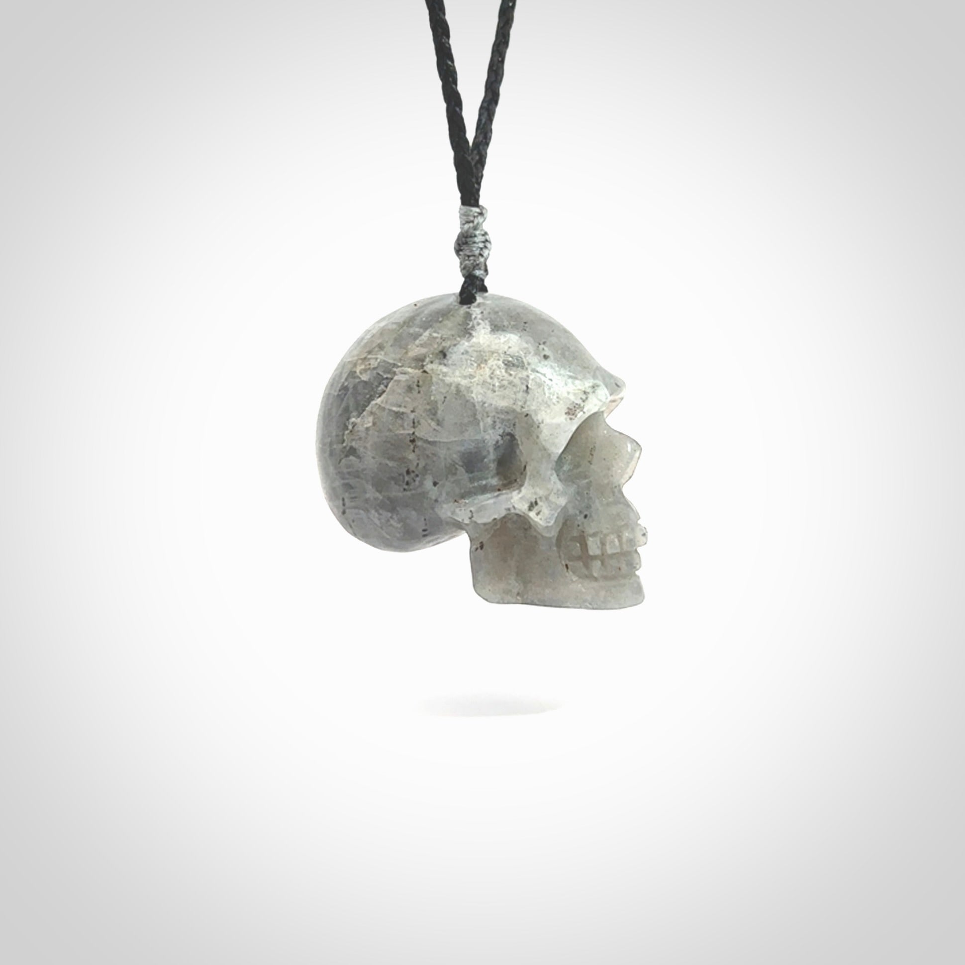 This picture shows a large sized Grey Moonstone skull pendant that we have hand carved. It is polished to a soft shine and is a very striking piece. The cord is black and has a small grey floret binding just above the pendant.