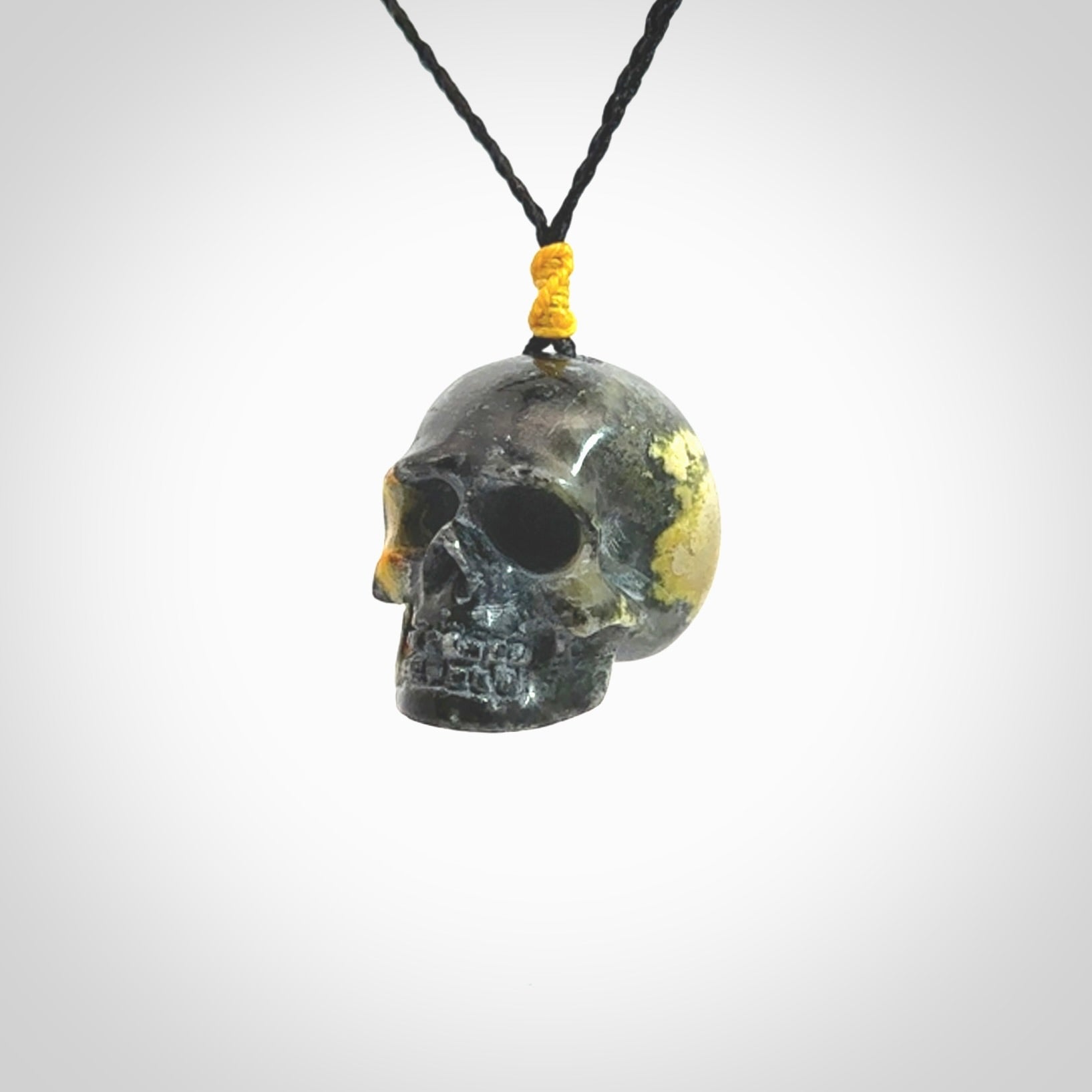 This picture shows a large sized Bumblebee Jasper stone skull pendant that we have hand carved. It is polished to a soft shine and is a very striking piece. The cord is a black colour and has a small yellow floret binding just above the pendant.