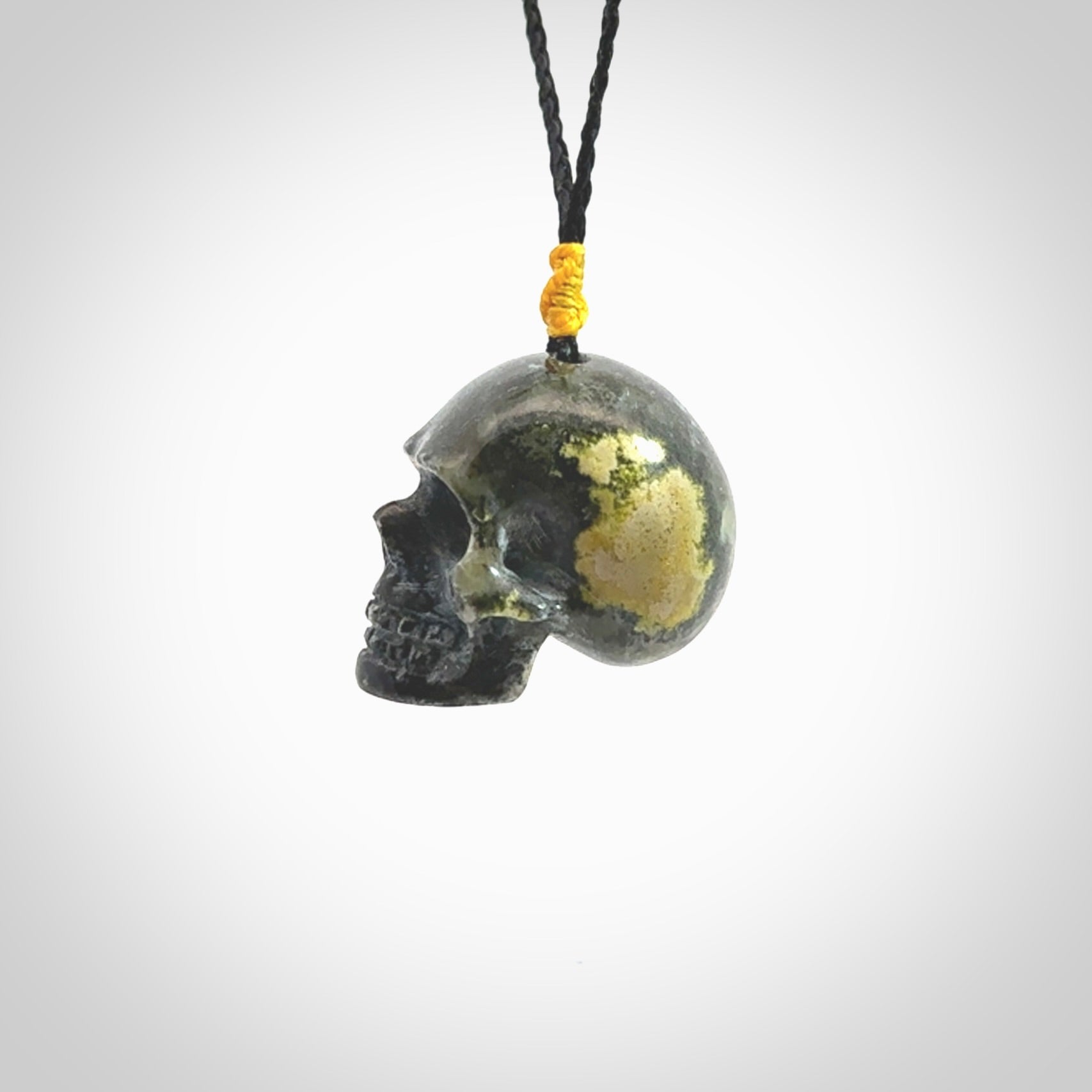 This picture shows a large sized Bumblebee Jasper stone skull pendant that we have hand carved. It is polished to a soft shine and is a very striking piece. The cord is a black colour and has a small yellow floret binding just above the pendant.