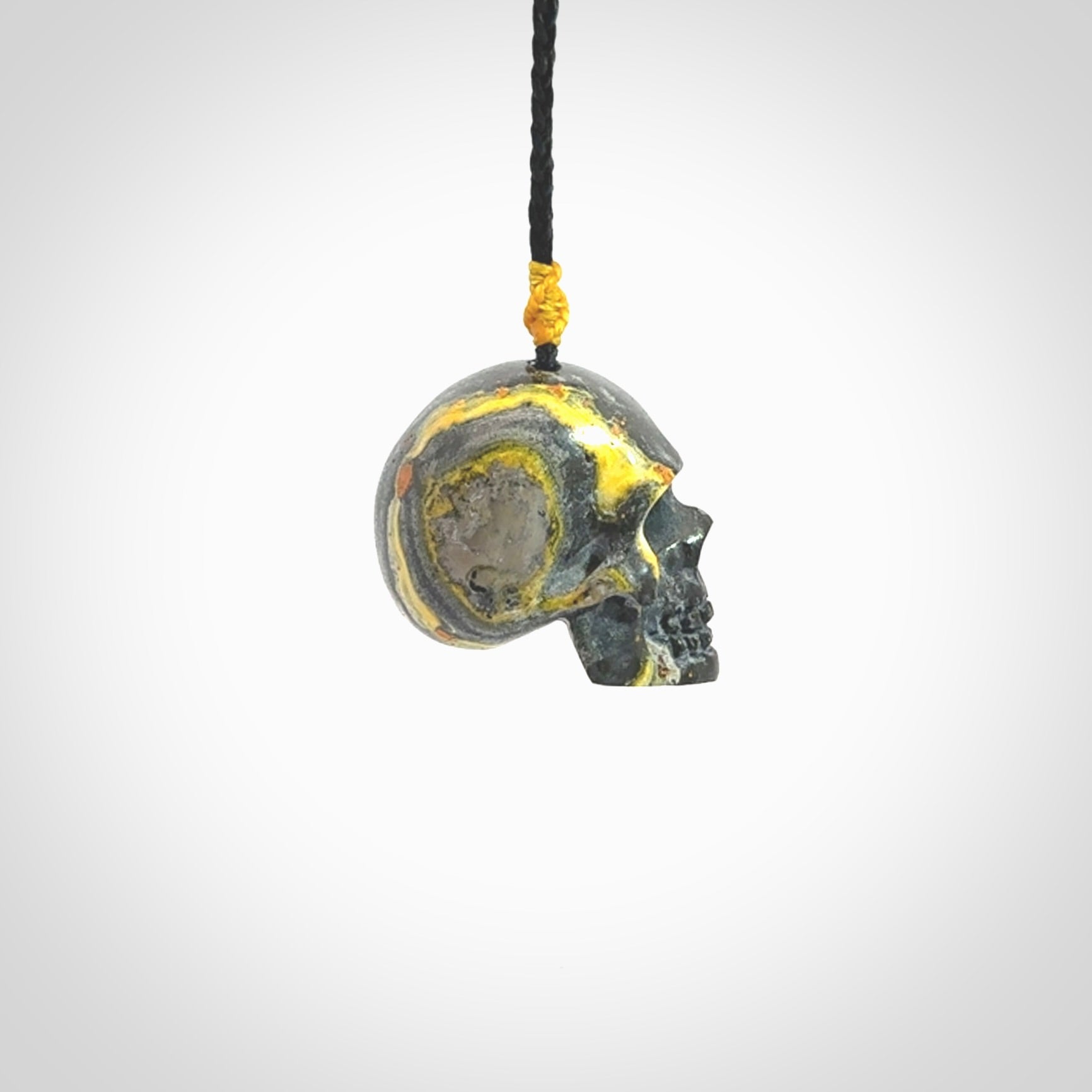 This picture shows a large sized Bumblebee Jasper stone skull pendant that we have hand carved. It is polished to a soft shine and is a very striking piece. The cord is a black colour and has a small yellow floret binding just above the pendant.