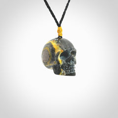 This picture shows a large sized Bumblebee Jasper stone skull pendant that we have hand carved. It is polished to a soft shine and is a very striking piece. The cord is a black colour and has a small yellow floret binding just above the pendant.