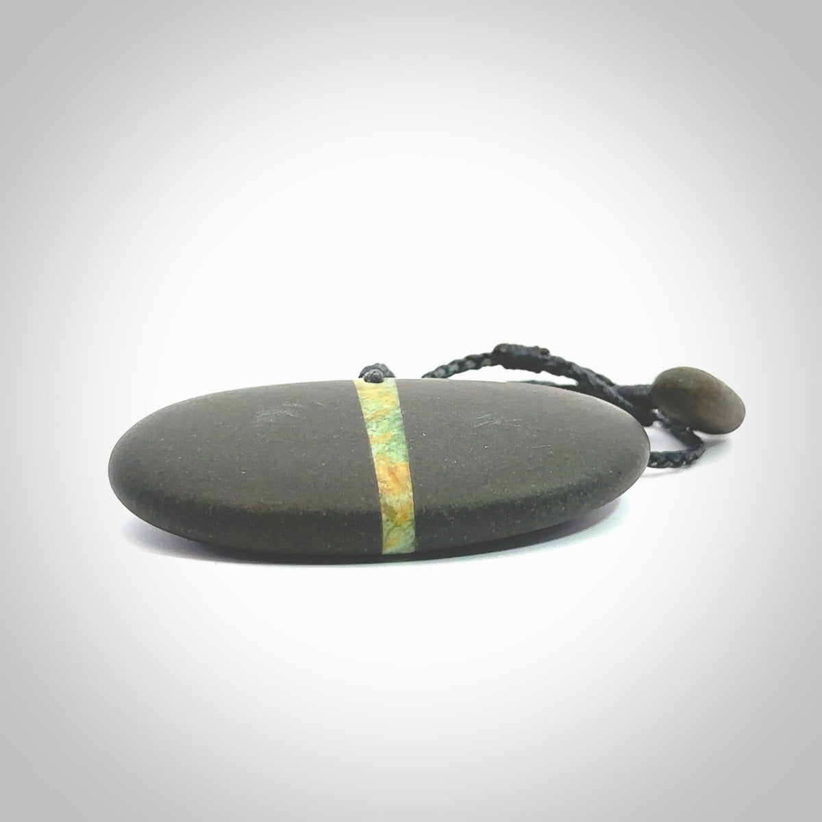 A drop pendant made from Onewa Stone - New Zealand Greywacke - with a fine Pounamu insert spliced into the middle. Hand carved stone drop with New Zealand Jade centre. Provided with an adjustable charcoal grey cord and packaged in a woven kete pouch.