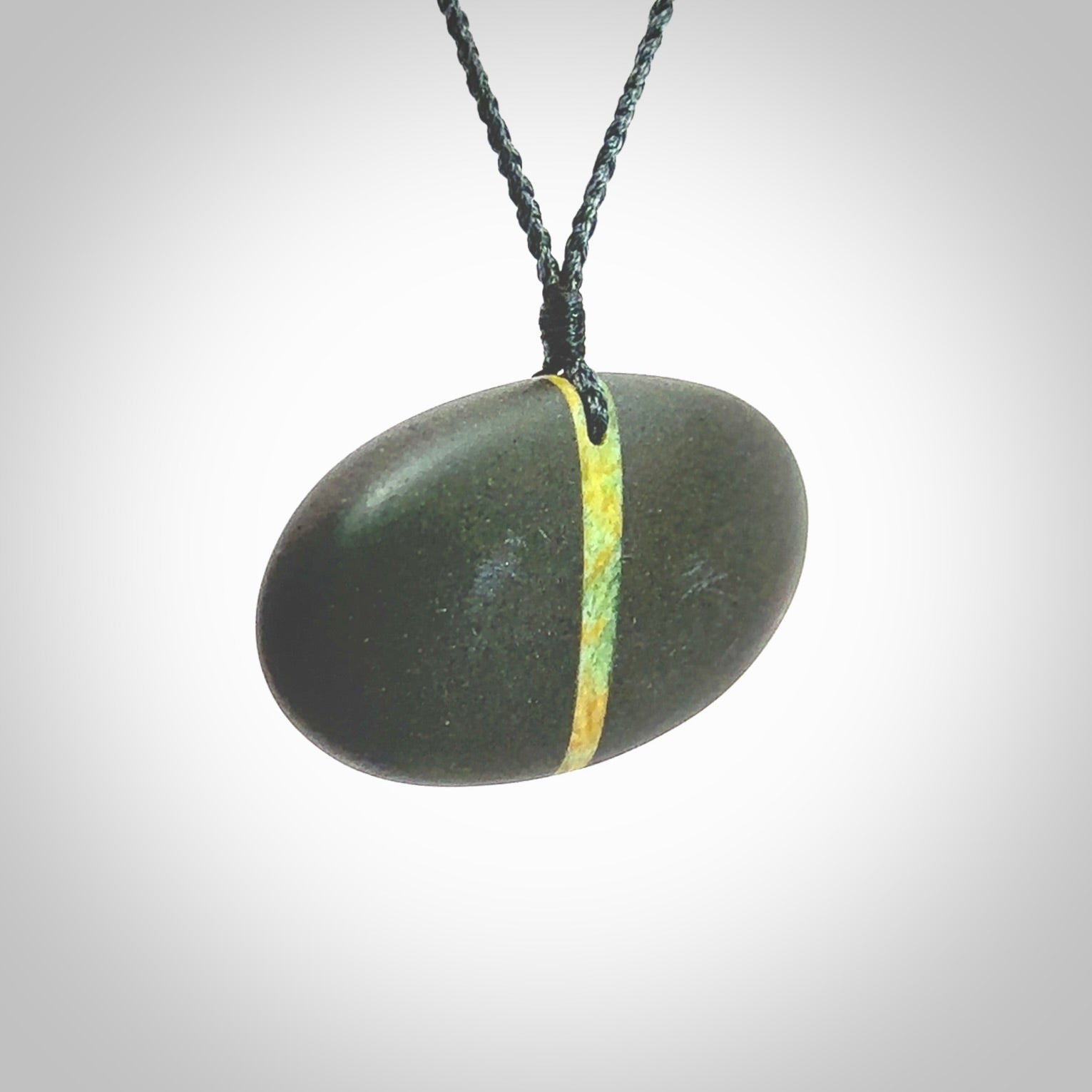 A drop pendant made from Onewa Stone - New Zealand Greywacke - with a fine Pounamu insert spliced into the middle. Hand carved stone drop with New Zealand Jade centre. Provided with an adjustable charcoal grey cord and packaged in a woven kete pouch.