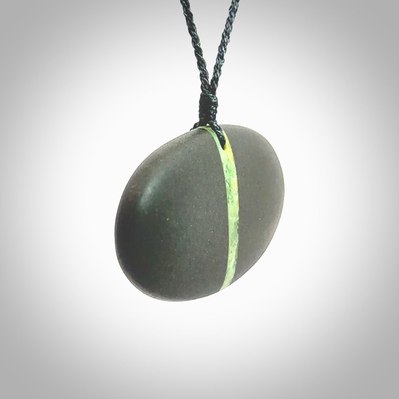 A drop pendant made from Onewa Stone - New Zealand Greywacke - with a fine Pounamu insert spliced into the middle. Hand carved stone drop with New Zealand Jade centre. Provided with an adjustable charcoal grey cord and packaged in a woven kete pouch.