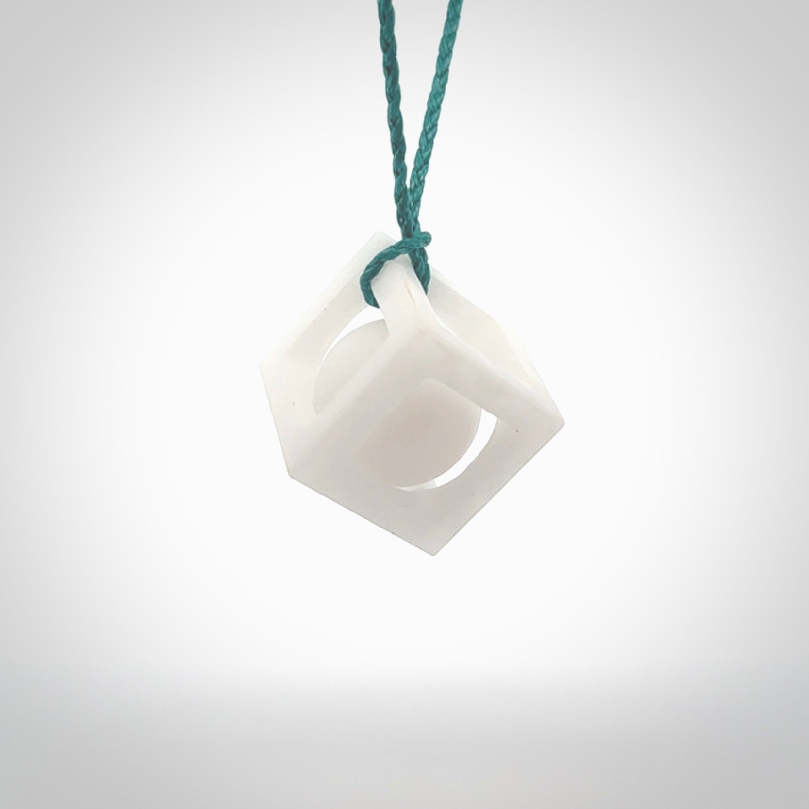 A hand carved medium sized white nephrite Jade square box with ball inside necklace. The cord is blue and adjustable in length. A medium sized hand made cube/box with ball necklace in white nephrite Jade stone. One off work of art to wear.