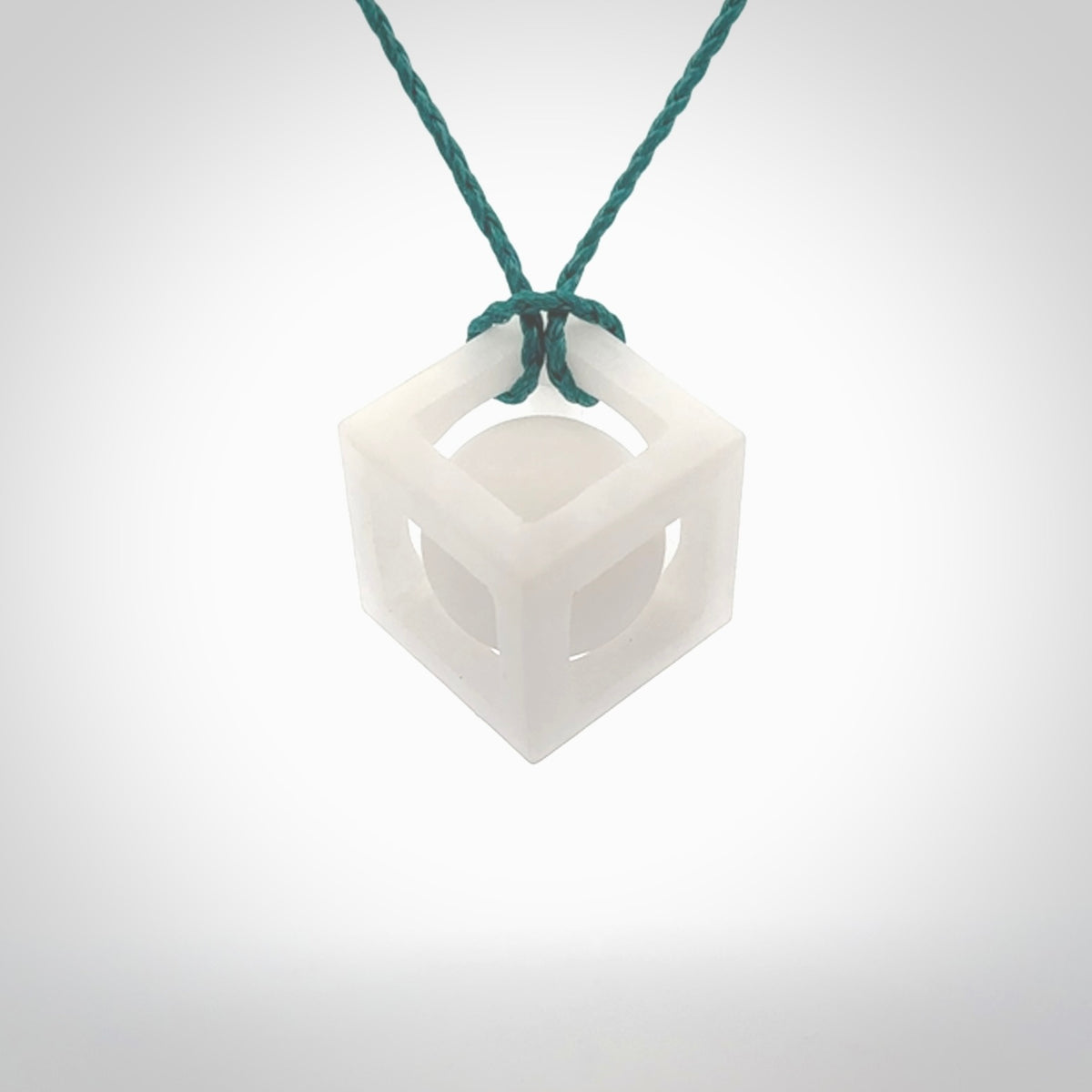 A hand carved medium sized white nephrite Jade square box with ball inside necklace. The cord is blue and adjustable in length. A medium sized hand made cube/box with ball necklace in white nephrite Jade stone. One off work of art to wear.