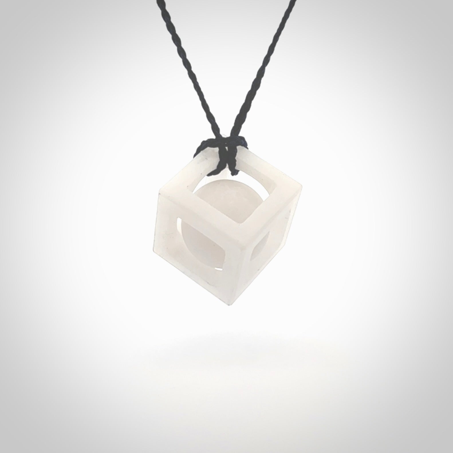 A hand carved medium sized white nephrite Jade square box with ball inside necklace. The cord is blue and adjustable in length. A medium sized hand made cube/box with ball necklace in white nephrite Jade stone. One off work of art to wear.