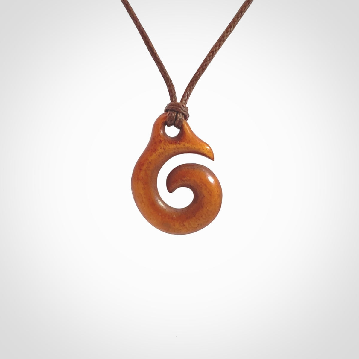 Stained natural cow bone hook with koru pendant. Hand carved by Yuri Terenyi in New Zealand. Koru design pendant for sale online. Stained bone koru necklace with adjustable brown cord. Free delivery worldwide.