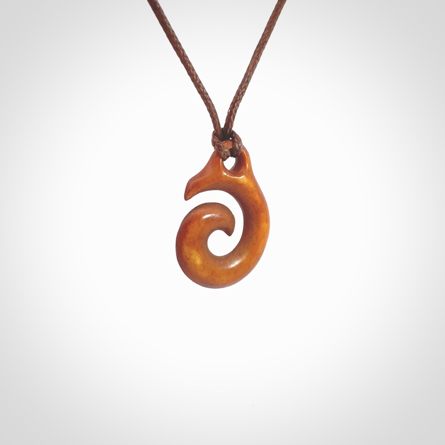 Stained natural cow bone hook with koru pendant. Hand carved by Yuri Terenyi in New Zealand. Koru design pendant for sale online. Stained bone koru necklace with adjustable brown cord. Free delivery worldwide.