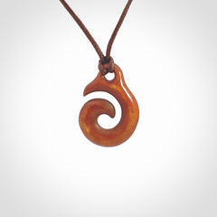 Stained natural cow bone hook with koru pendant. Hand carved by Yuri Terenyi in New Zealand. Koru design pendant for sale online. Stained bone koru necklace with adjustable brown cord. Free delivery worldwide.