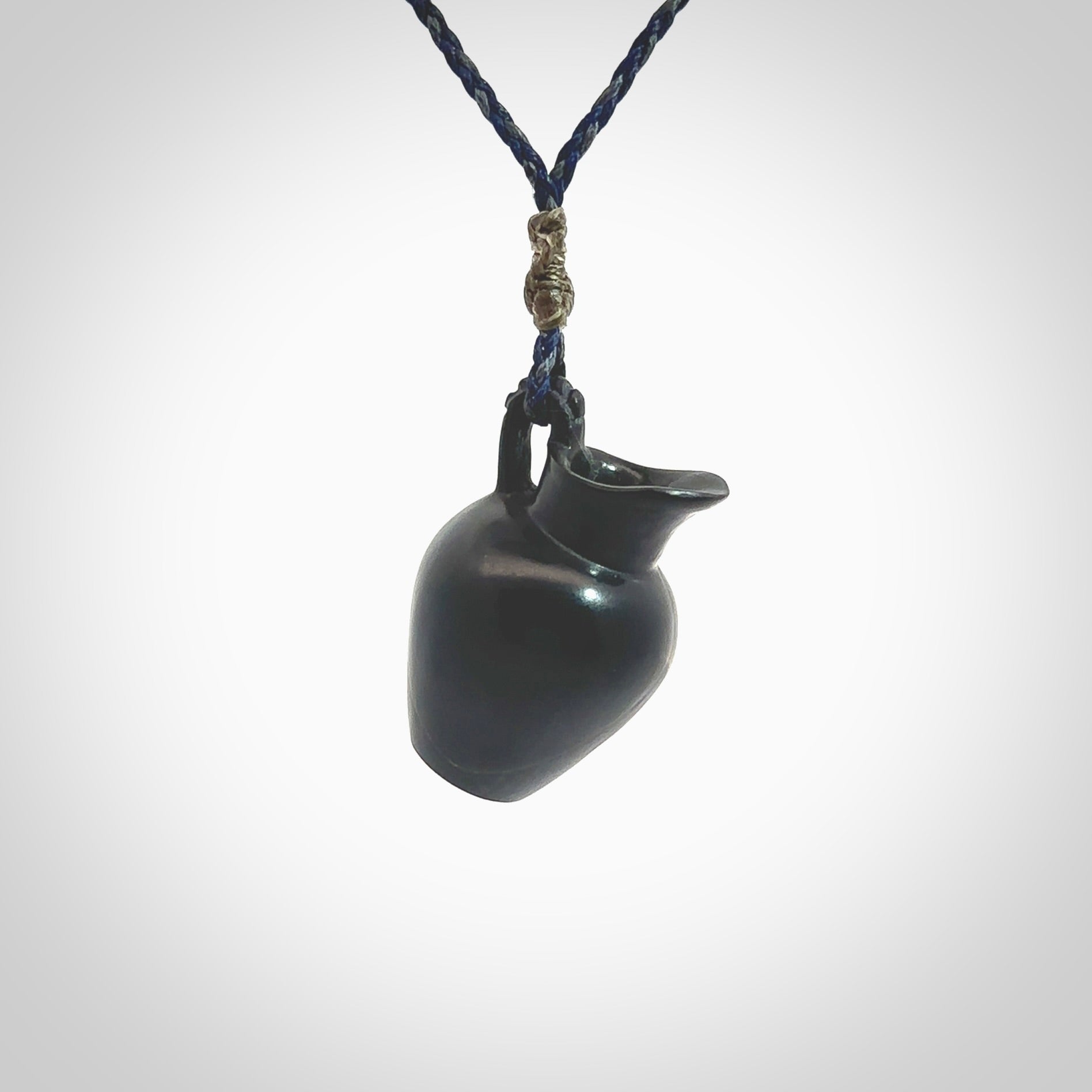 This picture shows a vase pendant that we designed in black jade. It is a black vase necklace that is carved in detail. A really attractive and eye-catching piece of handmade jewellery. The cord is hand plaited braid in charcoal grey and maui blue and the length can be adjusted. Delivered to you in a woven kete pouch and shipped with Express Courier.