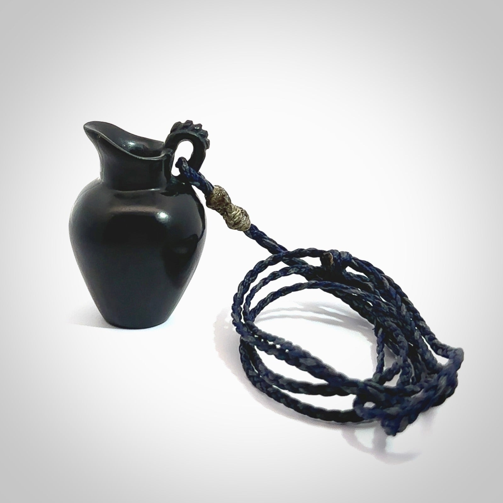 This picture shows a vase pendant that we designed in black jade. It is a black vase necklace that is carved in detail. A really attractive and eye-catching piece of handmade jewellery. The cord is hand plaited braid in charcoal grey and maui blue and the length can be adjusted. Delivered to you in a woven kete pouch and shipped with Express Courier.