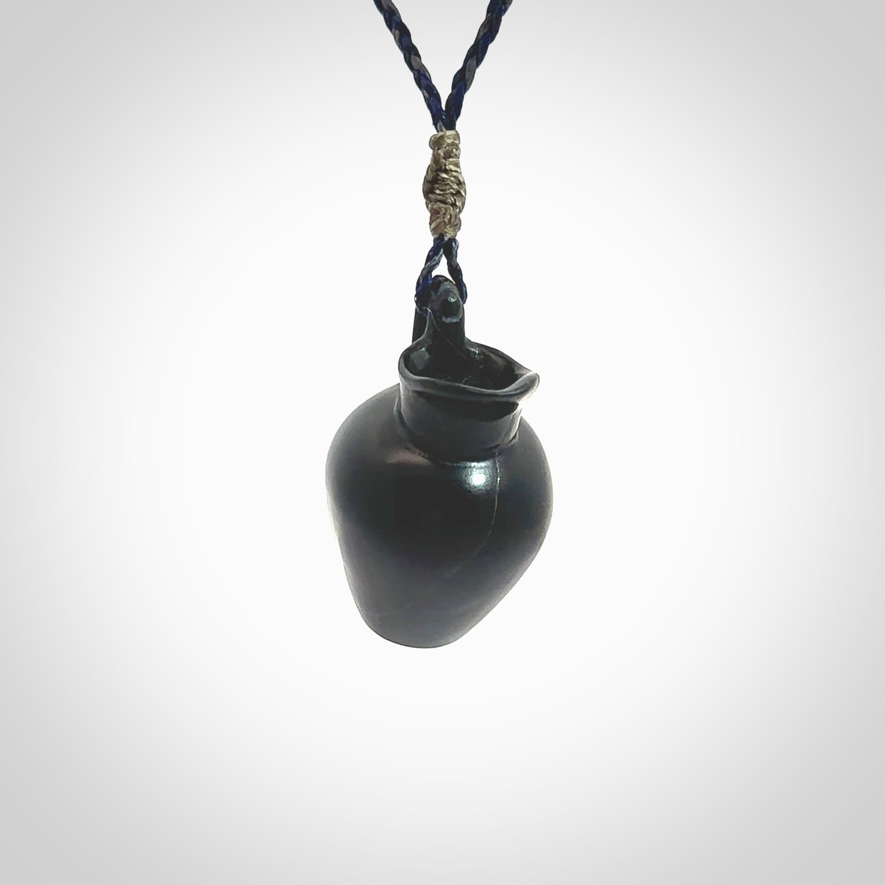 This picture shows a vase pendant that we designed in black jade. It is a black vase necklace that is carved in detail. A really attractive and eye-catching piece of handmade jewellery. The cord is hand plaited braid in charcoal grey and maui blue and the length can be adjusted. Delivered to you in a woven kete pouch and shipped with Express Courier.