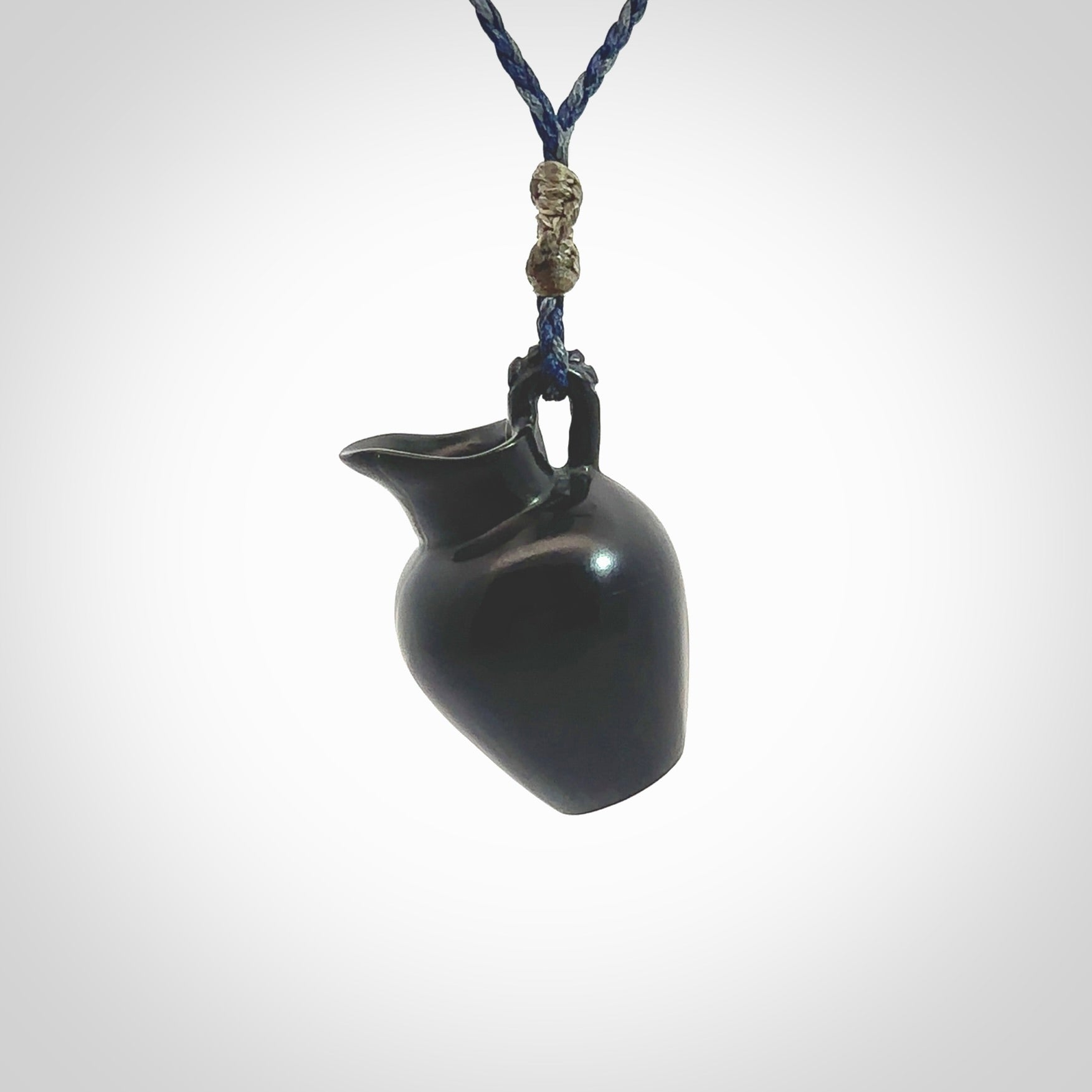 This picture shows a vase pendant that we designed in black jade. It is a black vase necklace that is carved in detail. A really attractive and eye-catching piece of handmade jewellery. The cord is hand plaited braid in charcoal grey and maui blue and the length can be adjusted. Delivered to you in a woven kete pouch and shipped with Express Courier.