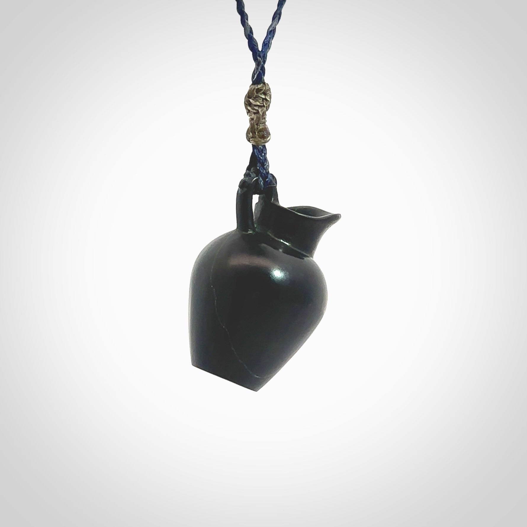 This picture shows a vase pendant that we designed in black jade. It is a black vase necklace that is carved in detail. A really attractive and eye-catching piece of handmade jewellery. The cord is hand plaited braid in charcoal grey and maui blue and the length can be adjusted. Delivered to you in a woven kete pouch and shipped with Express Courier.