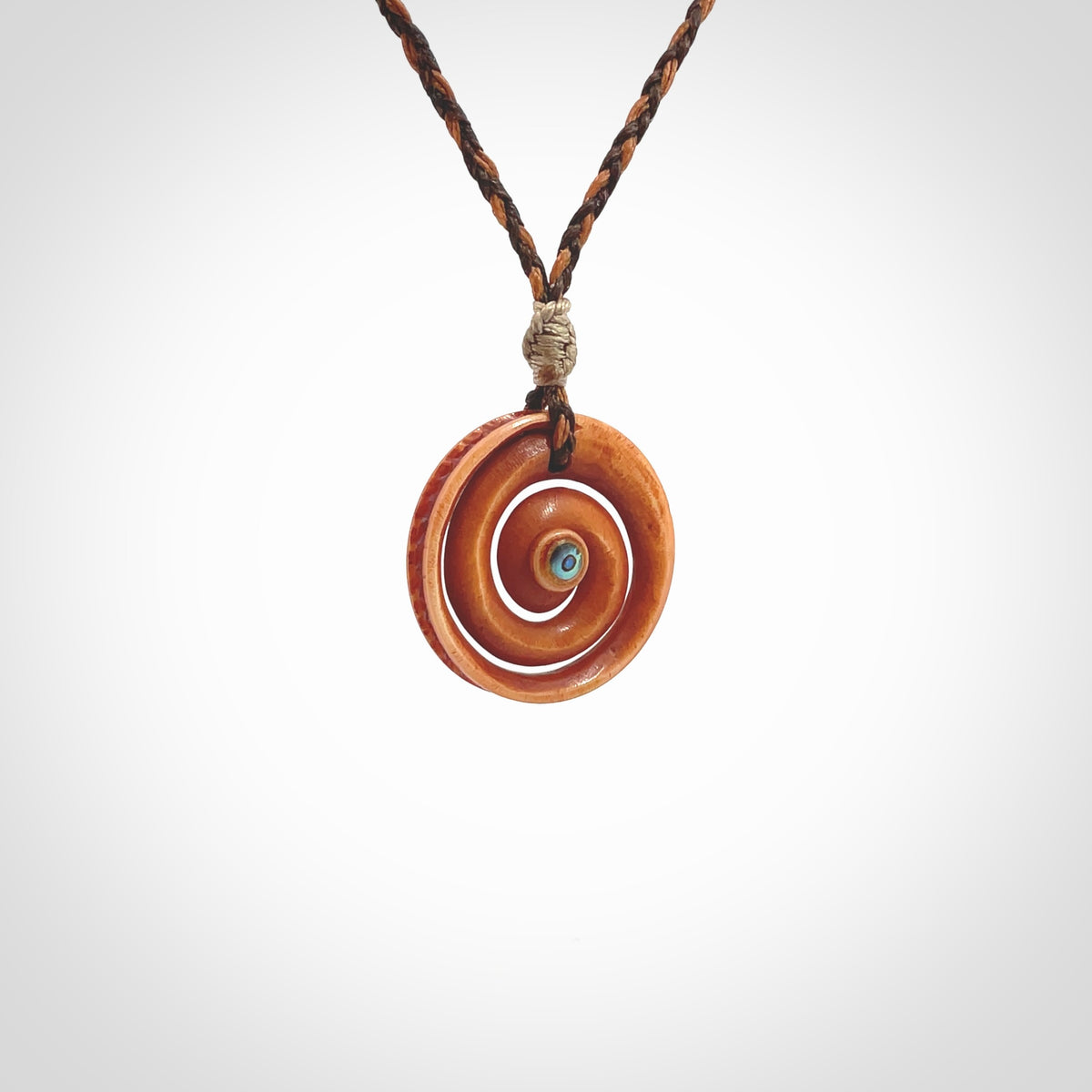 A hand carved and intricate koru pendant made for us by Yuri Terenyi. This is a beautiful little piece and is emblematic of the well known and loved Koru design. It is carved from stained bone in a hollowed, koru spiral shape with paua shell inlay in the middle of the koru. It is suspended from a gingernut brown/wapiti brown cord with a stardust floret and the necklace is adjustable.