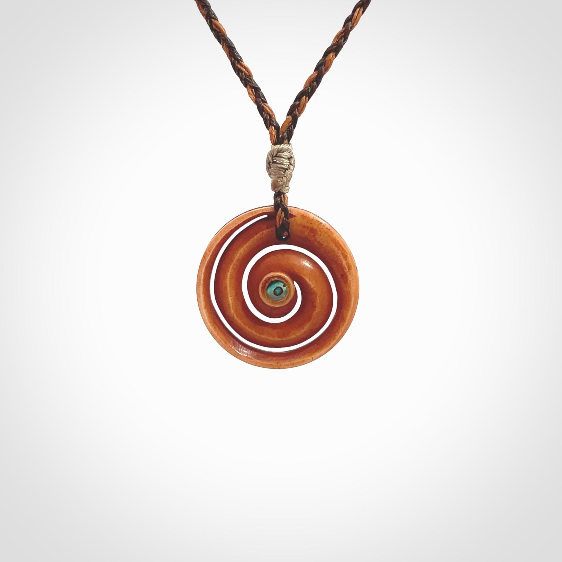 A hand carved and intricate koru pendant made for us by Yuri Terenyi. This is a beautiful little piece and is emblematic of the well known and loved Koru design. It is carved from stained bone in a hollowed, koru spiral shape with paua shell inlay in the middle of the koru. It is suspended from a gingernut brown/wapiti brown cord with a stardust floret and the necklace is adjustable.