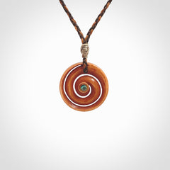 A hand carved and intricate koru pendant made for us by Yuri Terenyi. This is a beautiful little piece and is emblematic of the well known and loved Koru design. It is carved from stained bone in a hollowed, koru spiral shape with paua shell inlay in the middle of the koru. It is suspended from a gingernut brown/wapiti brown cord with a stardust floret and the necklace is adjustable.