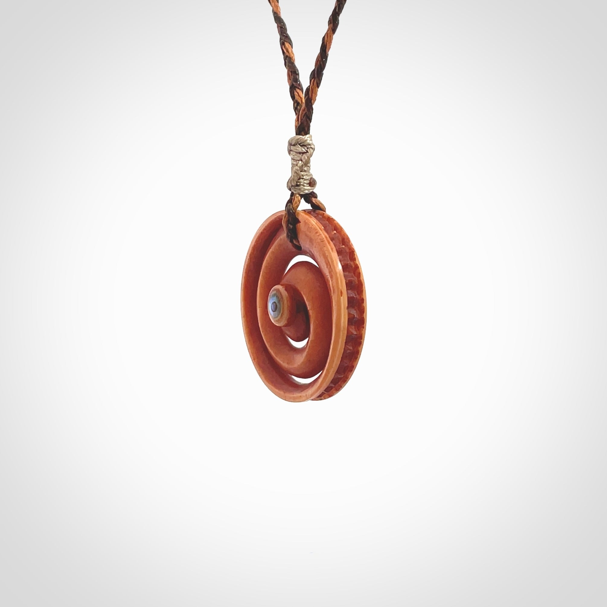 A hand carved and intricate koru pendant made for us by Yuri Terenyi. This is a beautiful little piece and is emblematic of the well known and loved Koru design. It is carved from stained bone in a hollowed, koru spiral shape with paua shell inlay in the middle of the koru. It is suspended from a gingernut brown/wapiti brown cord with a stardust floret and the necklace is adjustable.