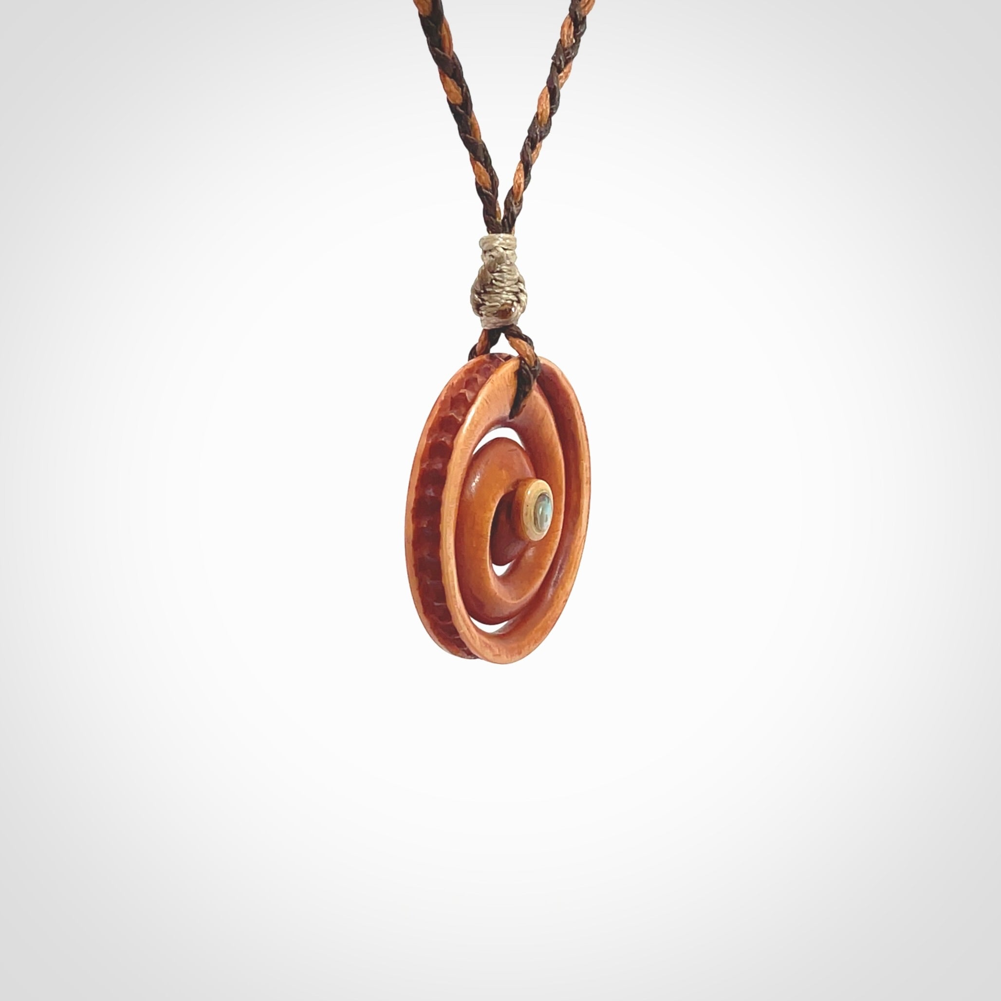 A hand carved and intricate koru pendant made for us by Yuri Terenyi. This is a beautiful little piece and is emblematic of the well known and loved Koru design. It is carved from stained bone in a hollowed, koru spiral shape with paua shell inlay in the middle of the koru. It is suspended from a gingernut brown/wapiti brown cord with a stardust floret and the necklace is adjustable.