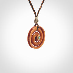 A hand carved and intricate koru pendant made for us by Yuri Terenyi. This is a beautiful little piece and is emblematic of the well known and loved Koru design. It is carved from stained bone in a hollowed, koru spiral shape with paua shell inlay in the middle of the koru. It is suspended from a gingernut brown/wapiti brown cord with a stardust floret and the necklace is adjustable.