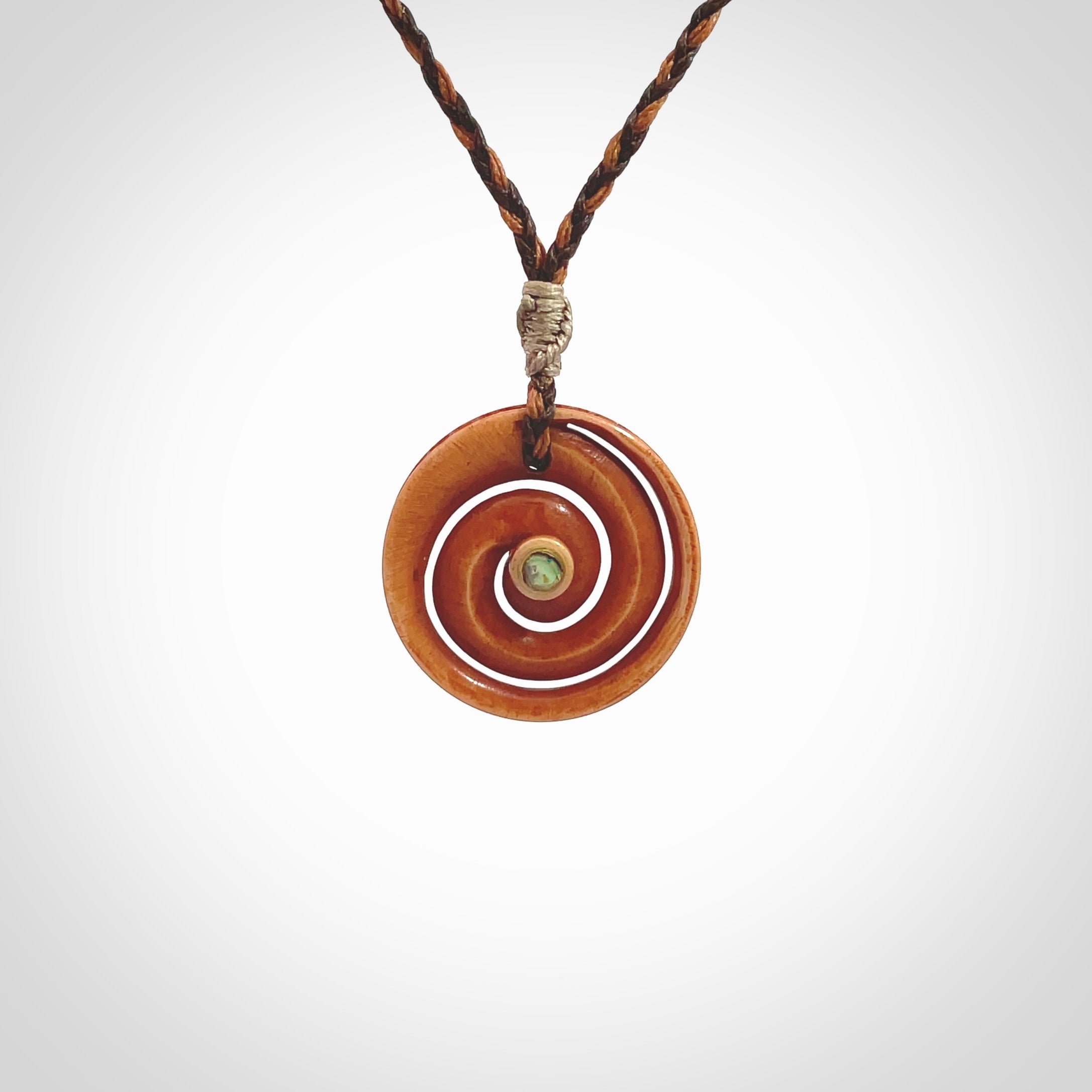 A hand carved and intricate koru pendant made for us by Yuri Terenyi. This is a beautiful little piece and is emblematic of the well known and loved Koru design. It is carved from stained bone in a hollowed, koru spiral shape with paua shell inlay in the middle of the koru. It is suspended from a gingernut brown/wapiti brown cord with a stardust floret and the necklace is adjustable.