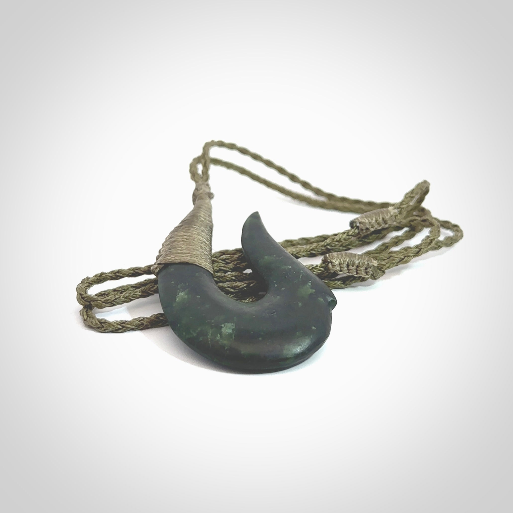 This photo shows a greenstone hook, or matau, pendant. It is a beautiful deep green jade. The cord is plaited olive green and the length can be adjusted.