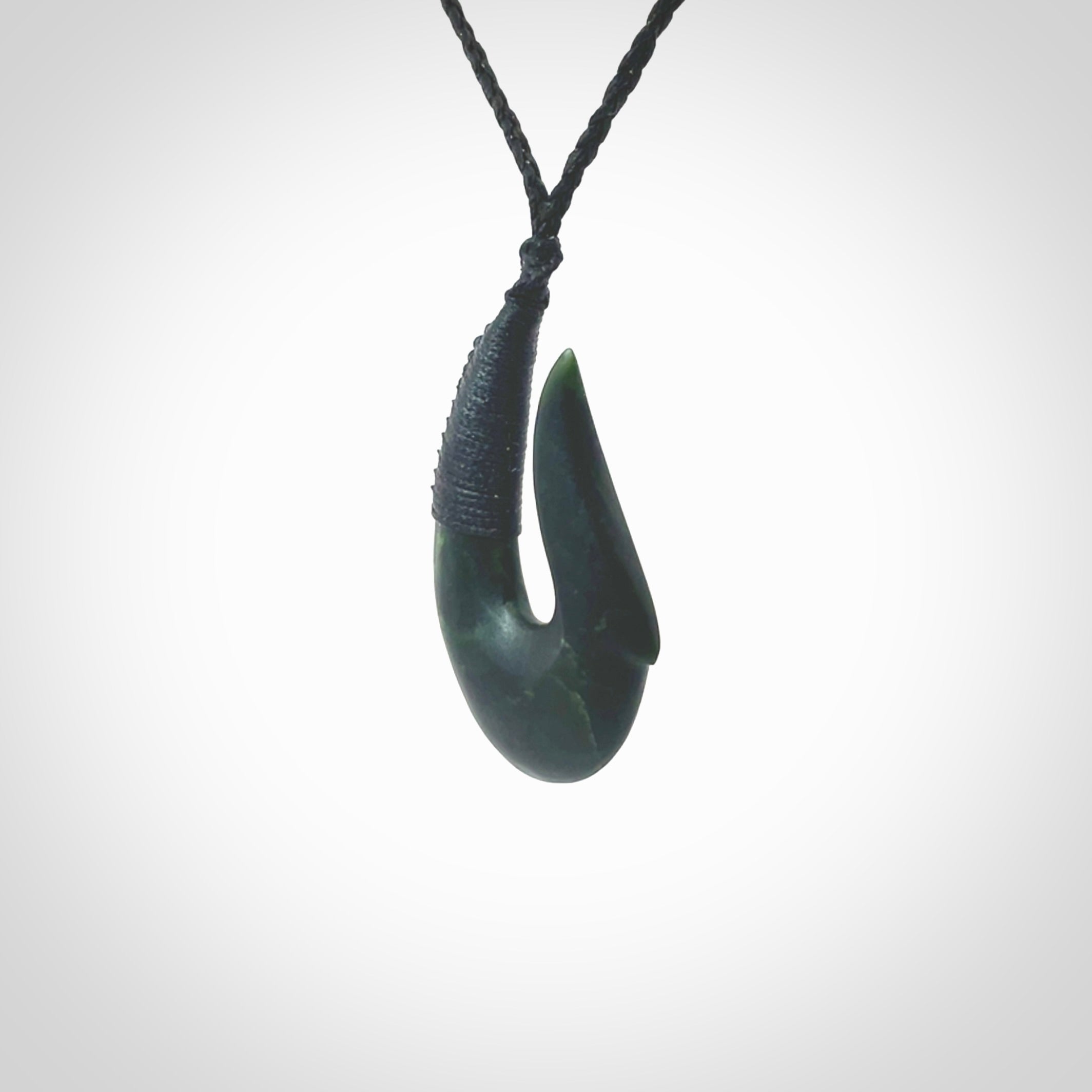 This photo shows a greenstone hook, or matau, pendant. It is a beautiful deep green jade. The cord is plaited in black and the length can be adjusted.