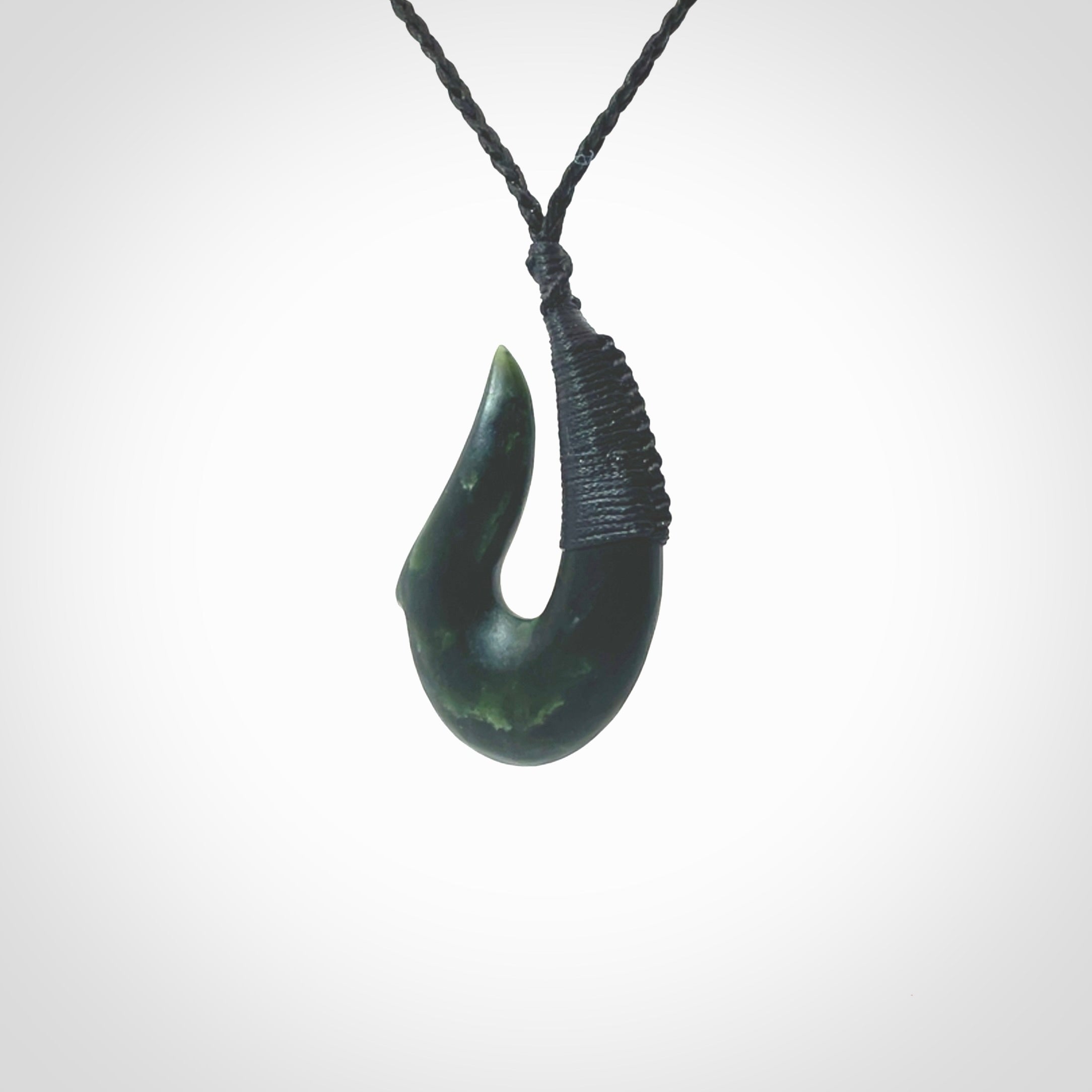 This photo shows a greenstone hook, or matau, pendant. It is a beautiful deep green jade. The cord is plaited in black and the length can be adjusted.