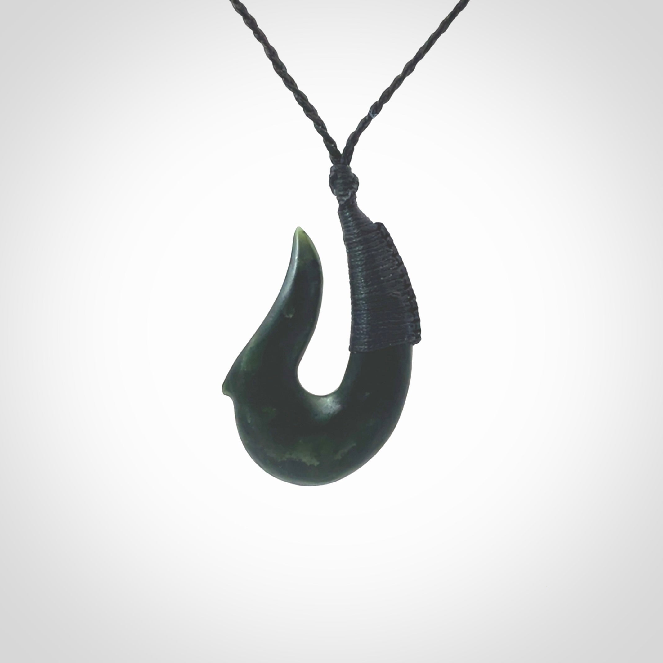 This photo shows a greenstone hook, or matau, pendant. It is a beautiful deep green jade. The cord is plaited in black and the length can be adjusted.