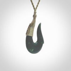 This photo shows a greenstone hook, or matau, pendant. It is a beautiful deep green jade. The cord is plaited olive green and the length can be adjusted.