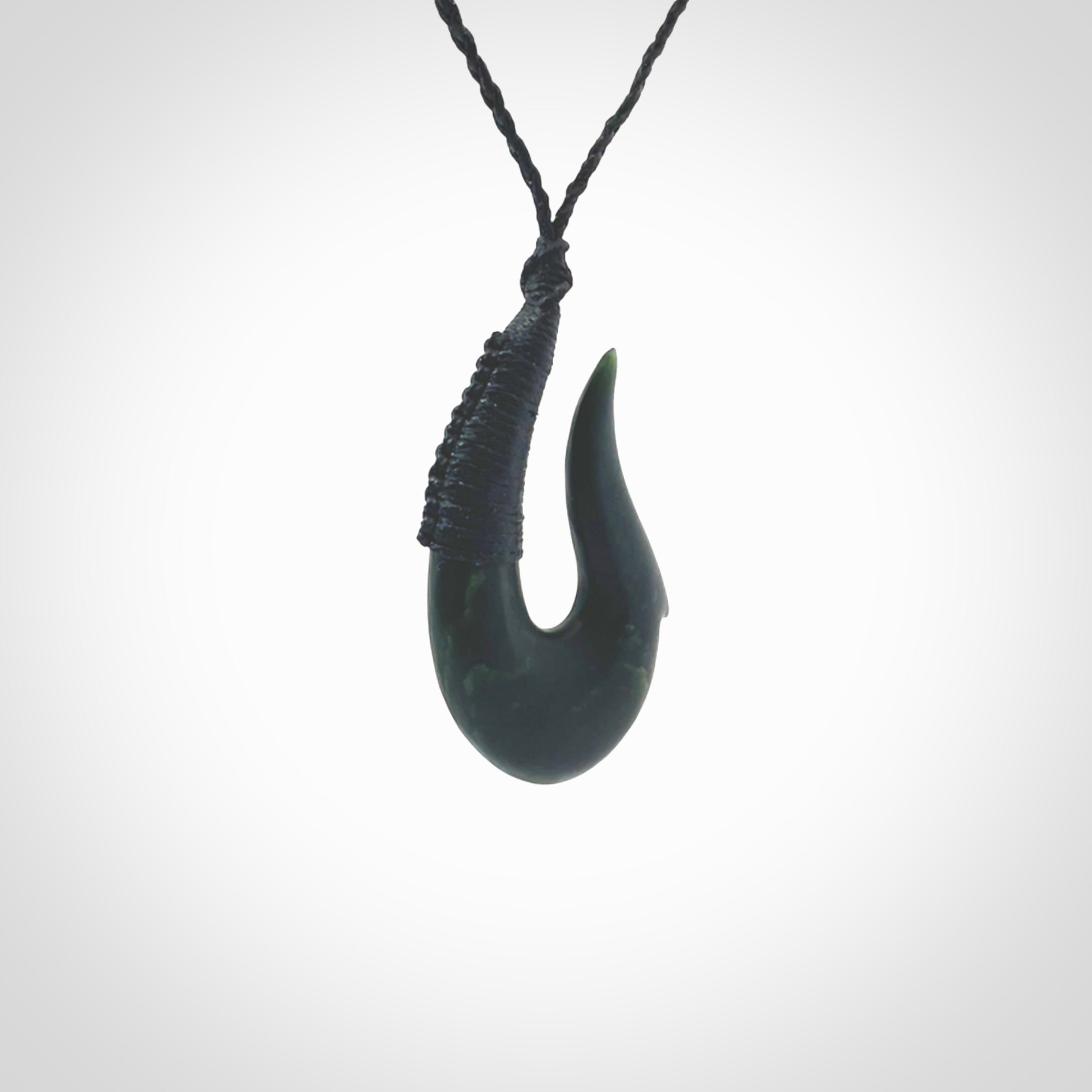 This photo shows a greenstone hook, or matau, pendant. It is a beautiful deep green jade. The cord is plaited in black and the length can be adjusted.