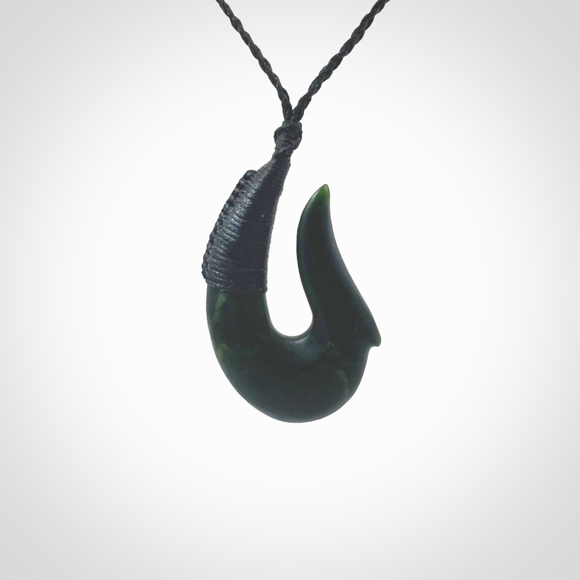 This photo shows a greenstone hook, or matau, pendant. It is a beautiful deep green jade. The cord is plaited in black and the length can be adjusted.