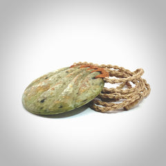 This picture shows a hand carved sea shell disc pendant made from a flowering green/orange coloured flower jade. Hand made by Ana Krakosky. It is provided with an adjustable 4-Plait Kalahari tan cord and chestnut brown binding. Delivered to you with Express Courier.