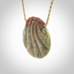 This picture shows a hand carved sea shell disc pendant made from a flowering green/orange coloured flower jade. Hand made by Ana Krakosky. It is provided with an adjustable 4-Plait Kalahari tan cord and chestnut brown binding. Delivered to you with Express Courier.