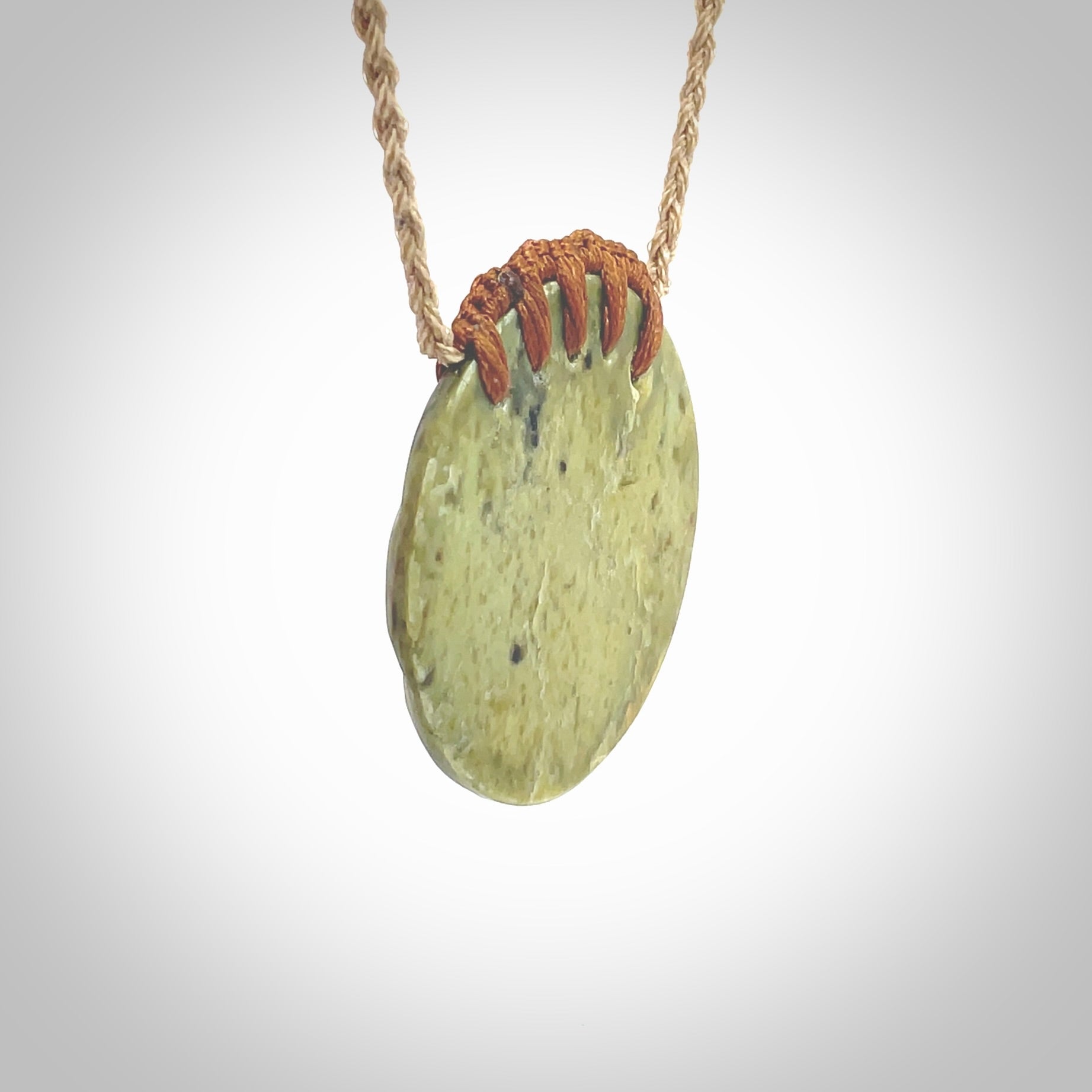 This picture shows a hand carved sea shell disc pendant made from a flowering green/orange coloured flower jade. Hand made by Ana Krakosky. It is provided with an adjustable 4-Plait Kalahari tan cord and chestnut brown binding. Delivered to you with Express Courier.