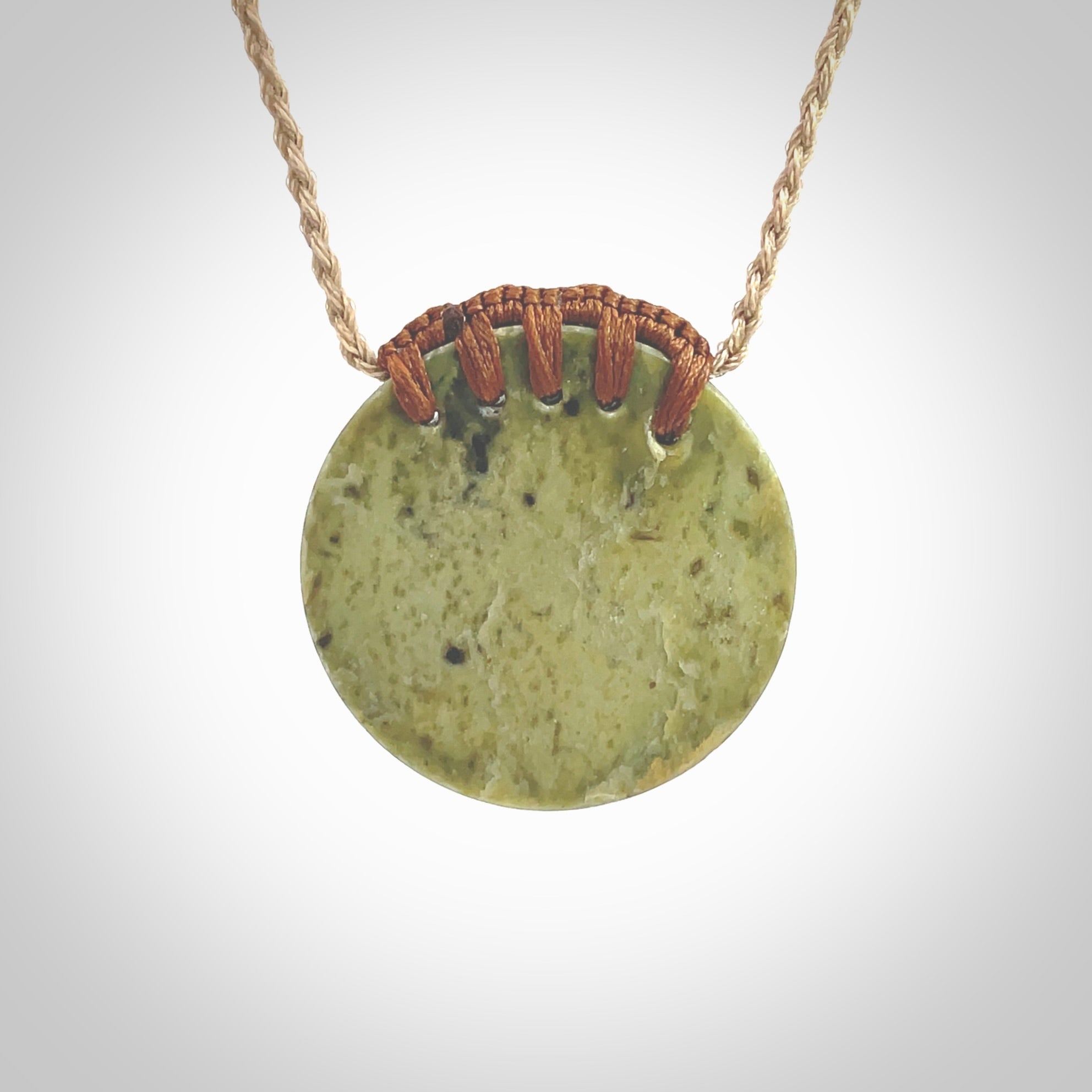 This picture shows a hand carved sea shell disc pendant made from a flowering green/orange coloured flower jade. Hand made by Ana Krakosky. It is provided with an adjustable 4-Plait Kalahari tan cord and chestnut brown binding. Delivered to you with Express Courier.