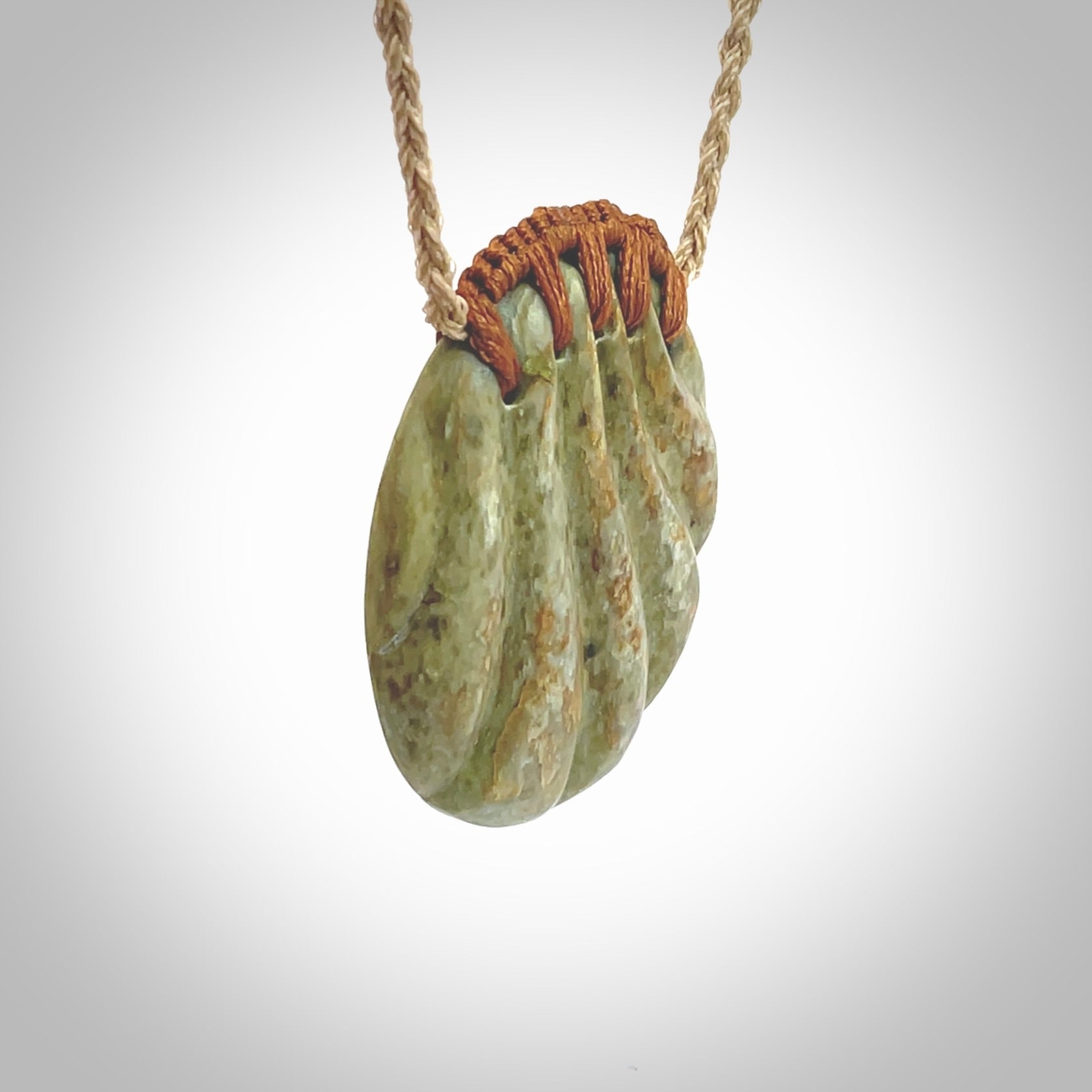 This picture shows a hand carved sea shell disc pendant made from a flowering green/orange coloured flower jade. Hand made by Ana Krakosky. It is provided with an adjustable 4-Plait Kalahari tan cord and chestnut brown binding. Delivered to you with Express Courier.