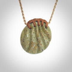 This picture shows a hand carved sea shell disc pendant made from a flowering green/orange coloured flower jade. Hand made by Ana Krakosky. It is provided with an adjustable 4-Plait Kalahari tan cord and chestnut brown binding. Delivered to you with Express Courier.