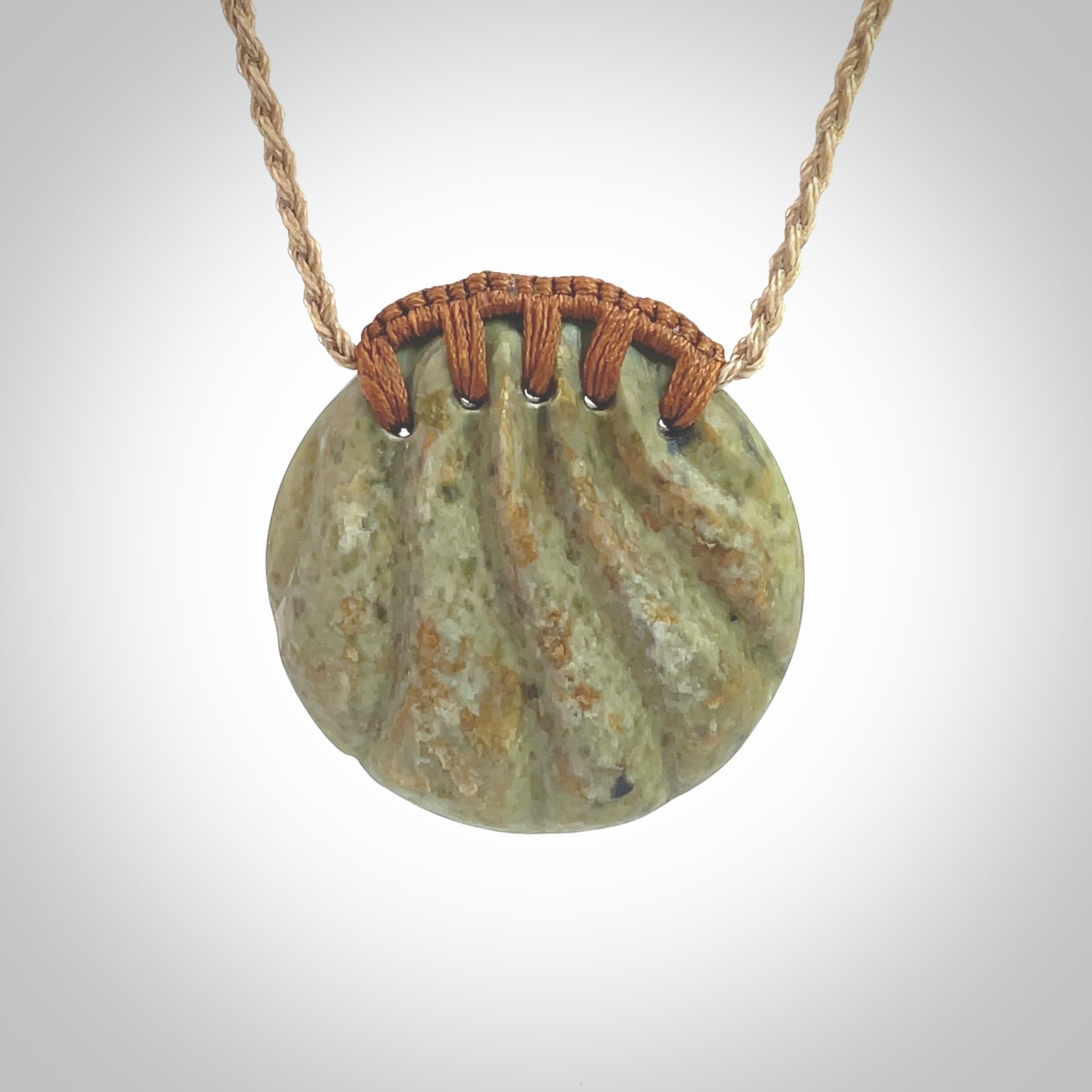 This picture shows a hand carved sea shell disc pendant made from a flowering green/orange coloured flower jade. Hand made by Ana Krakosky. It is provided with an adjustable 4-Plait Kalahari tan cord and chestnut brown binding. Delivered to you with Express Courier.