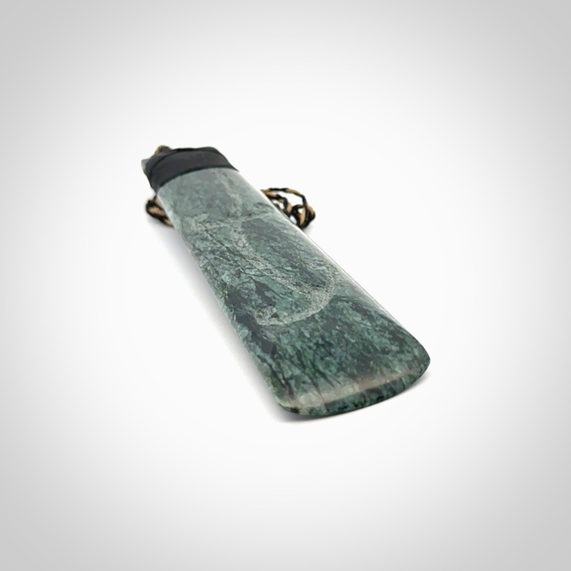 Large New Zealand Tangiwai Pounamu Toki pendant with Tangiwai boulder display case. Hand carved from a lovely piece of local New Zealand Tangiwai Stone. The quality of the workmanship and design is outstanding - this is a piece you will want to wear all the time. We have suspended this from an adjustable 3-plait tan/black cord.