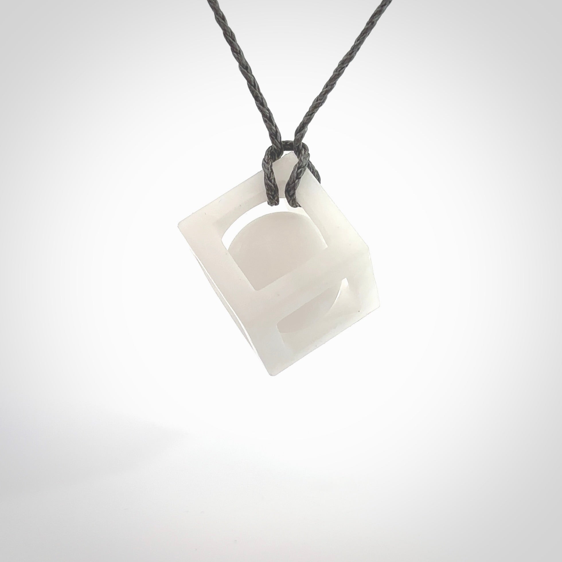 A hand carved medium sized white nephrite Jade square box with ball inside necklace. The cord is grey and adjustable in length. A medium sized hand made cube/box with ball necklace in white nephrite Jade stone. One off work of art to wear.